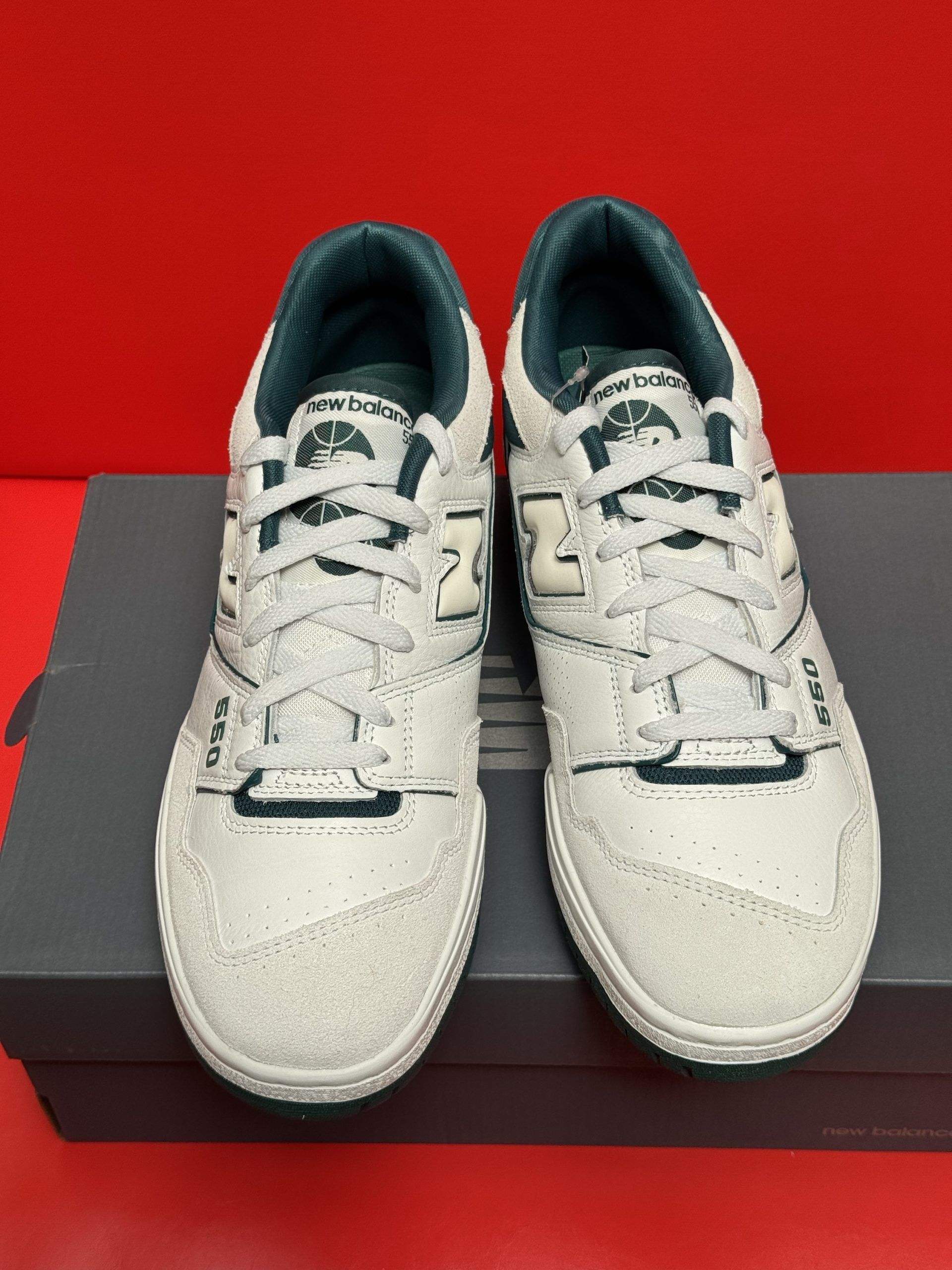 New Balance 550 sneakers, white leather, green accents, sitting atop a gray shoebox. Green sole visible.