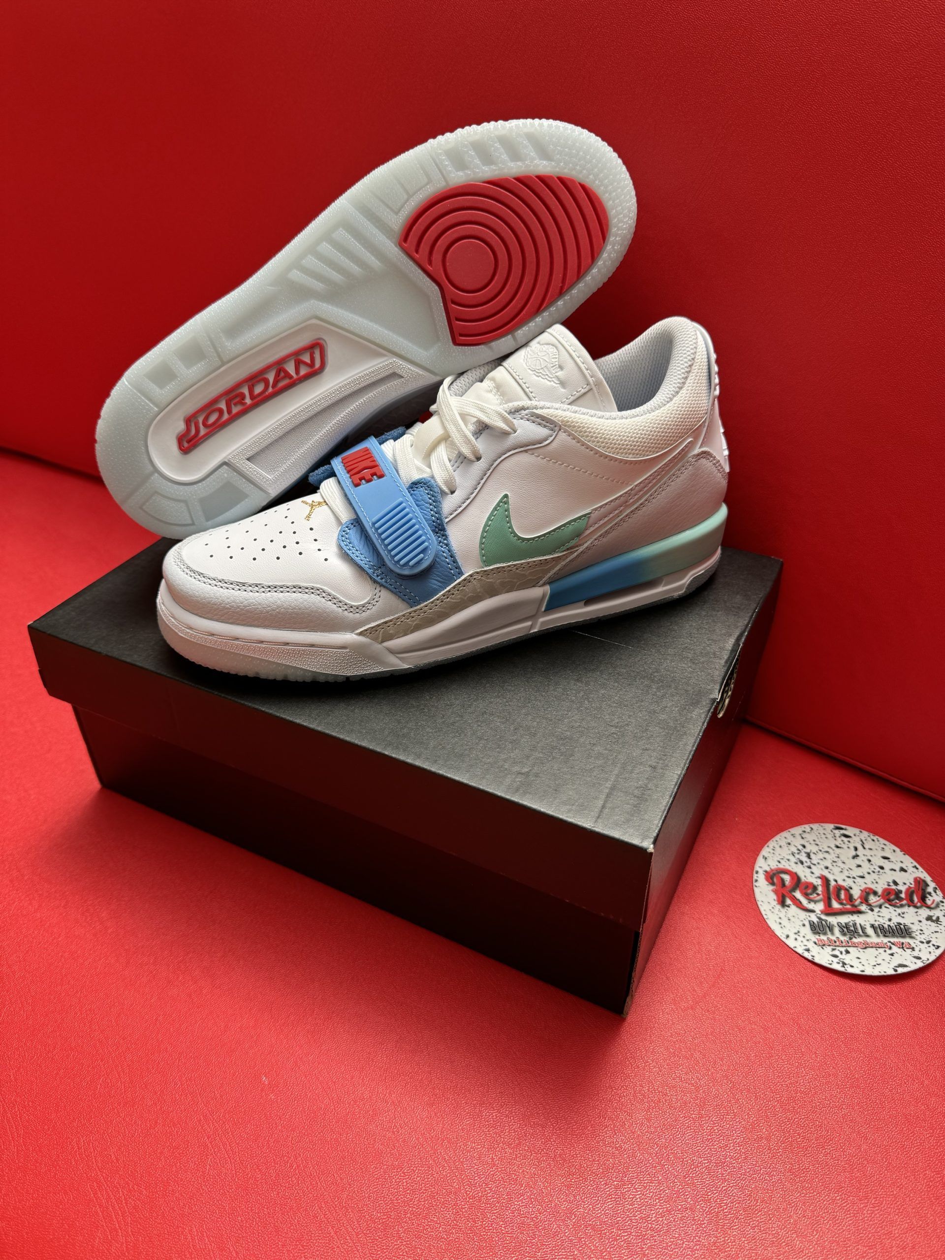 White and blue Jordan sneakers with a fuzzy texture, on a black box, and red background.