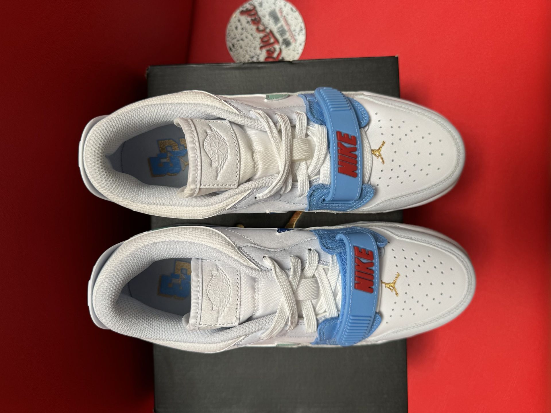 White and blue Jordan sneakers with a fuzzy texture, on a black box, and red background.