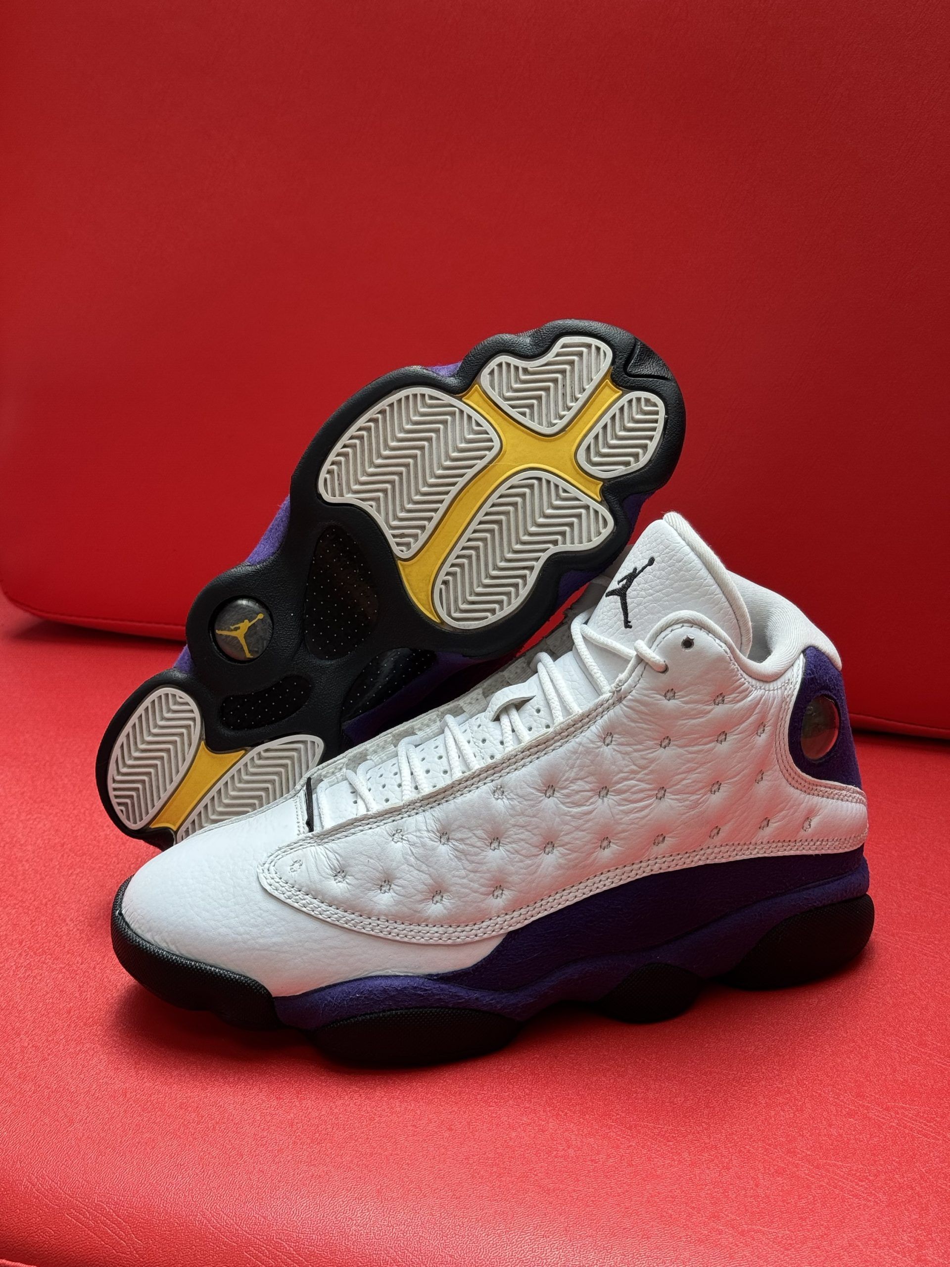 White and purple Air Jordan 13 sneakers on a red surface.