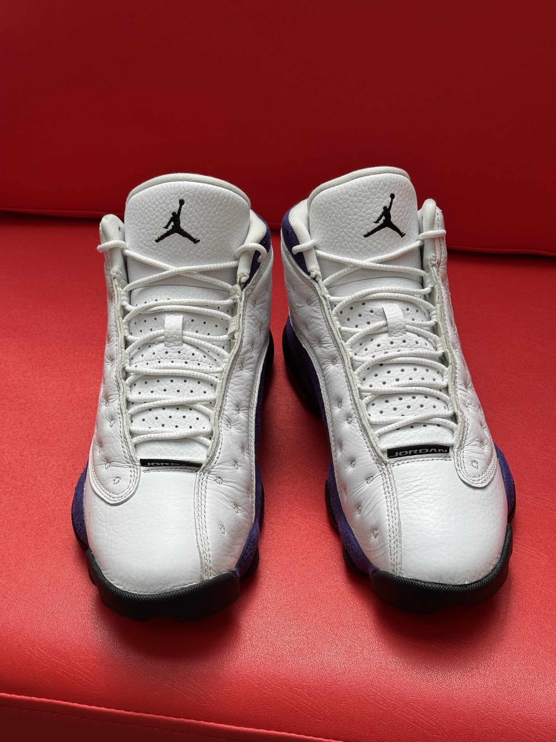 White and purple Air Jordan 13 sneakers on a red surface.