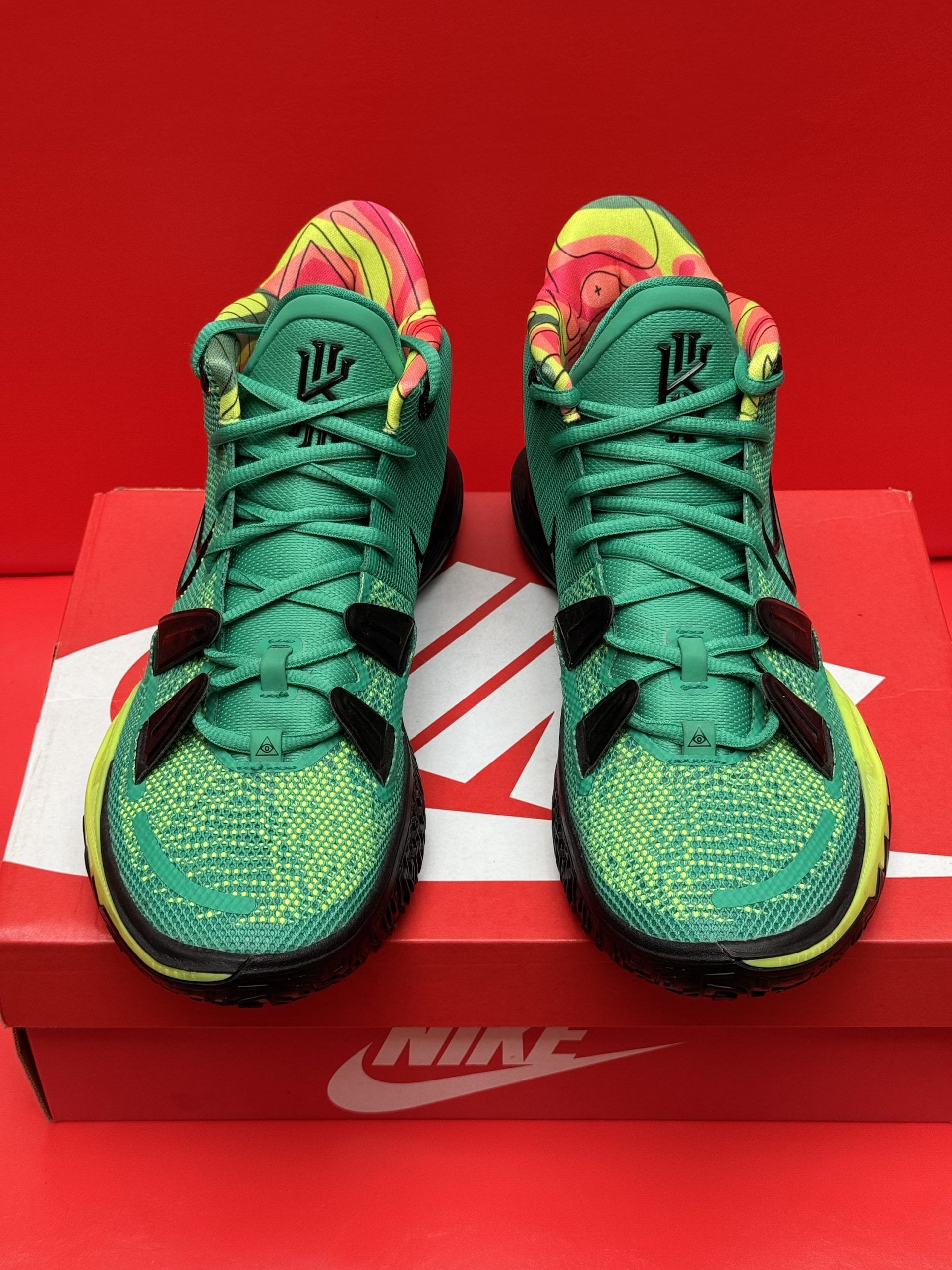 Green and black Nike Kyrie 7 basketball shoe on a box, sole visible, red background.