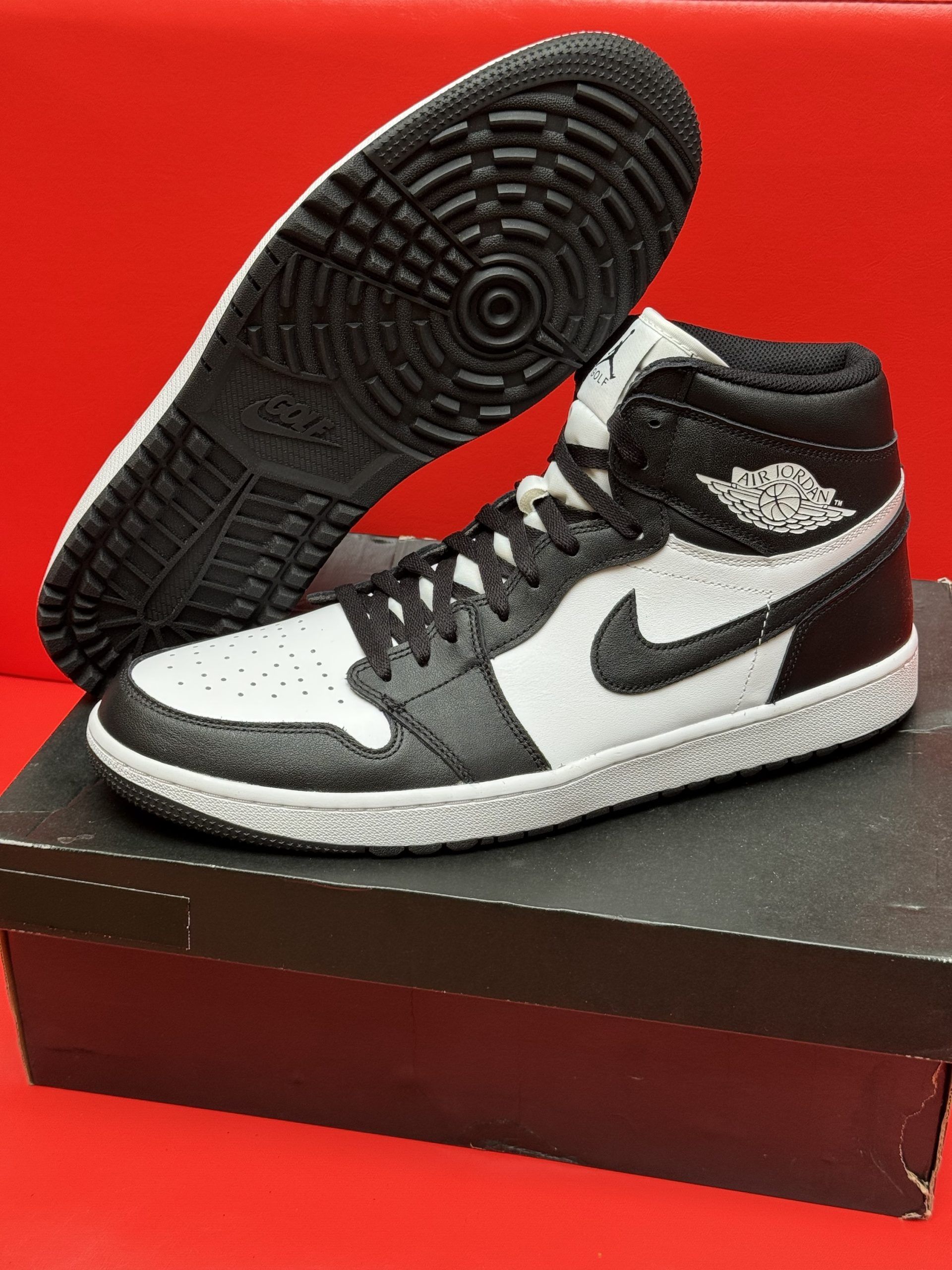 Black and white Air Jordan 1 sneaker on box, sole facing up. Red background.
