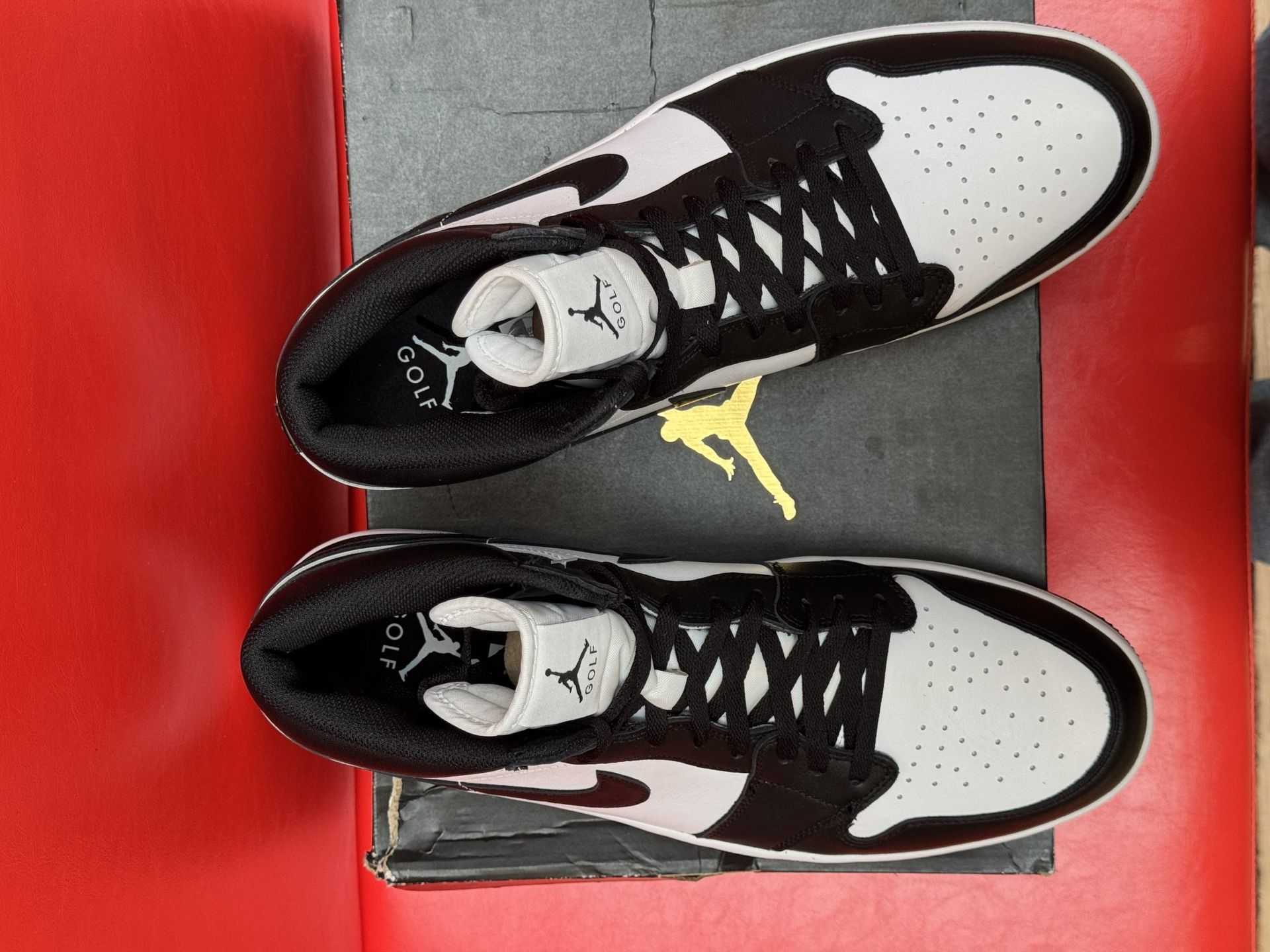 Black and white Air Jordan 1 sneaker on box, sole facing up. Red background.