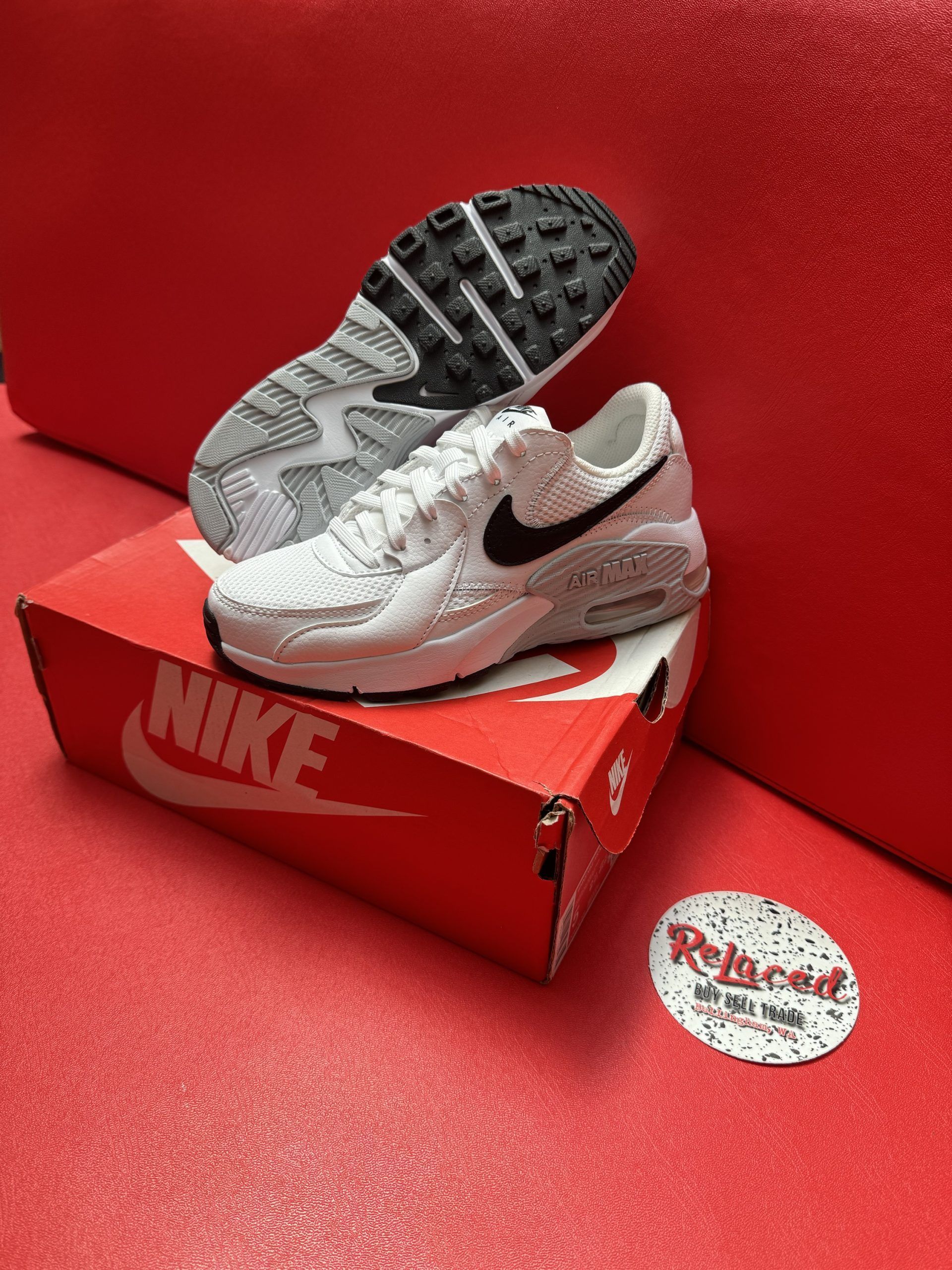 White Nike Air Max sneakers with black accents on a red Nike box, against a red background.