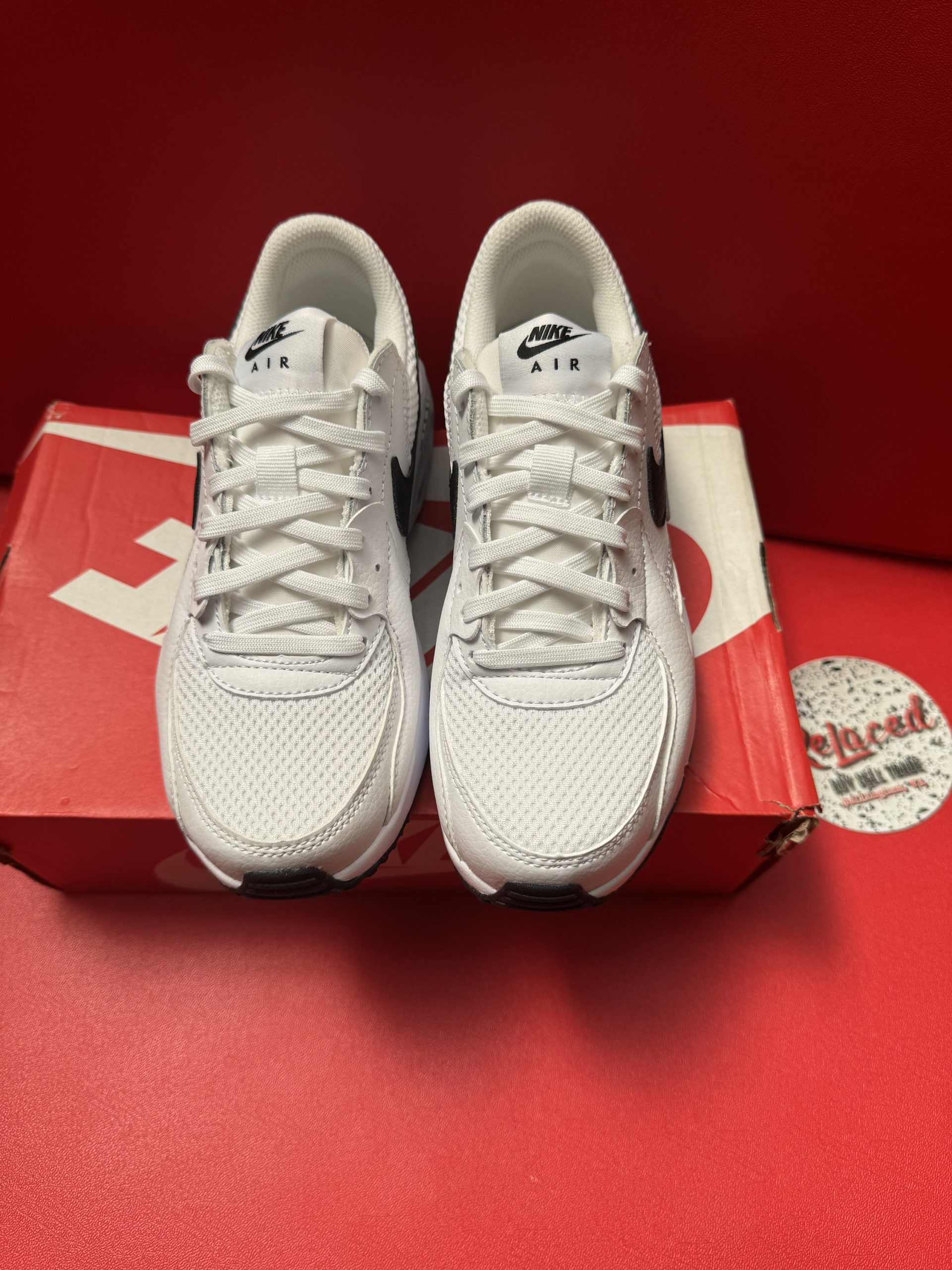 White Nike Air Max sneakers with black accents on a red Nike box, against a red background.