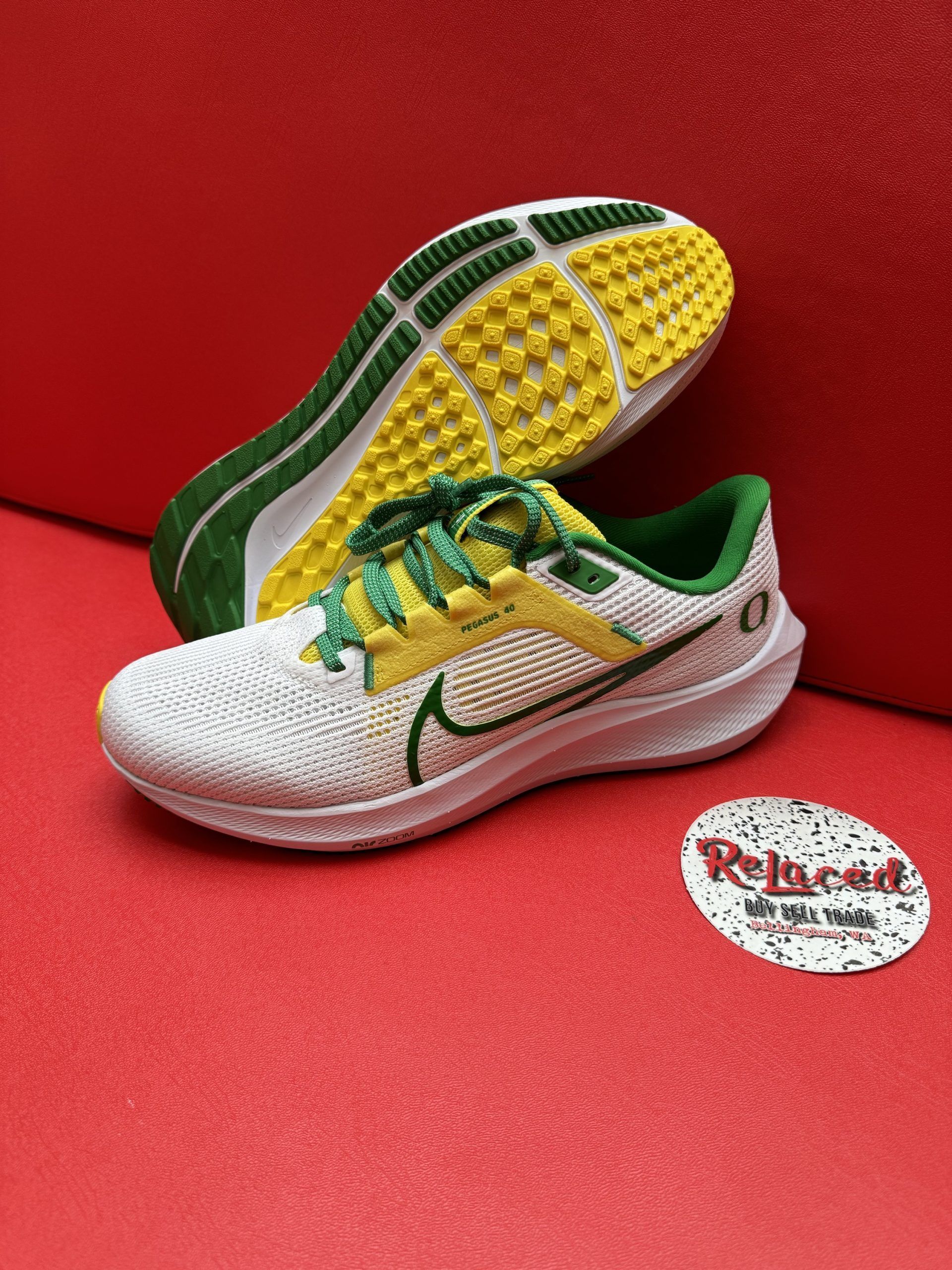 White and gold Nike running shoe with green accents, sole up showing yellow and green tread.