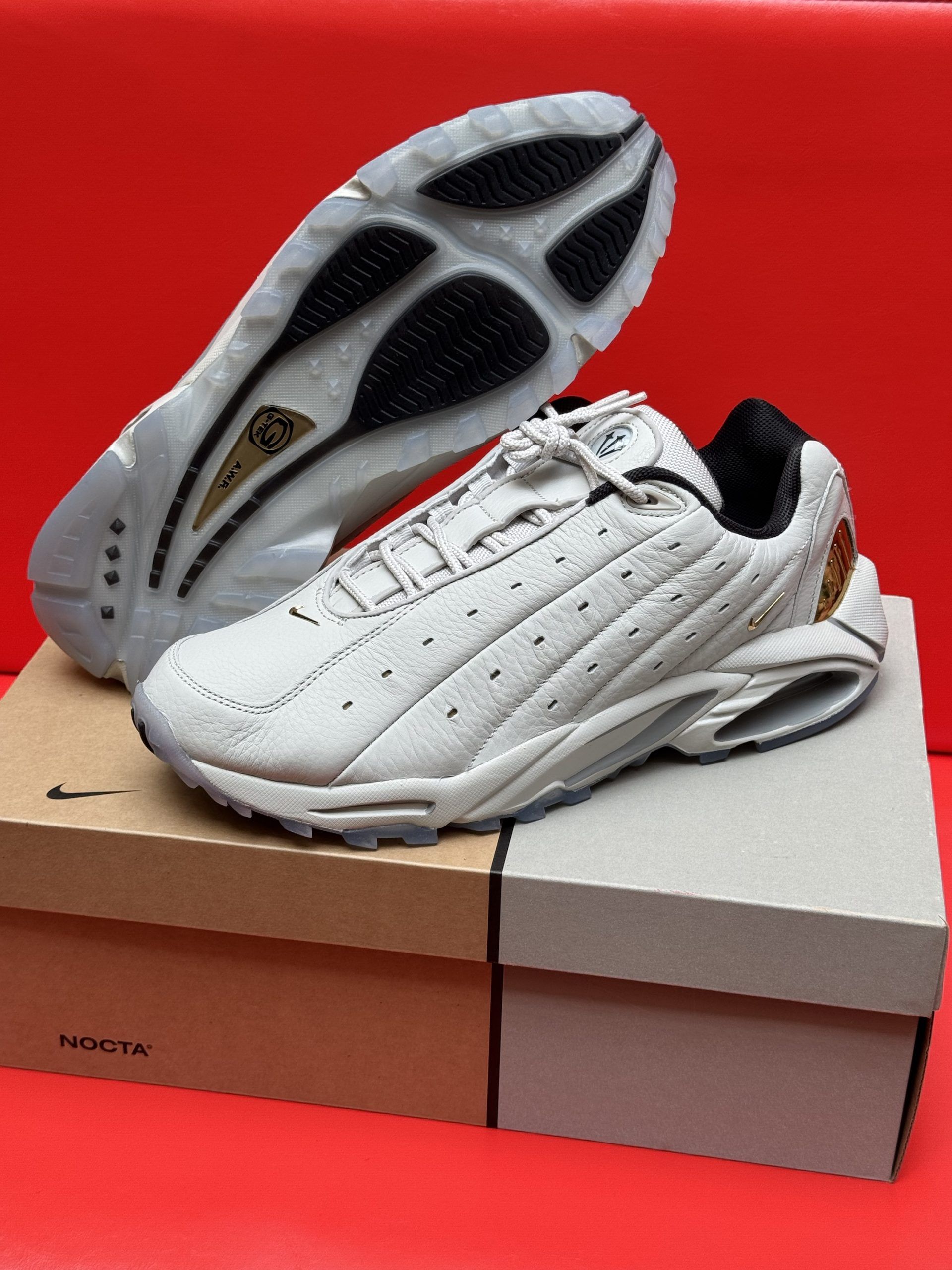 Beige Nike Air Max sneakers on box with sole visible, set against a red background.