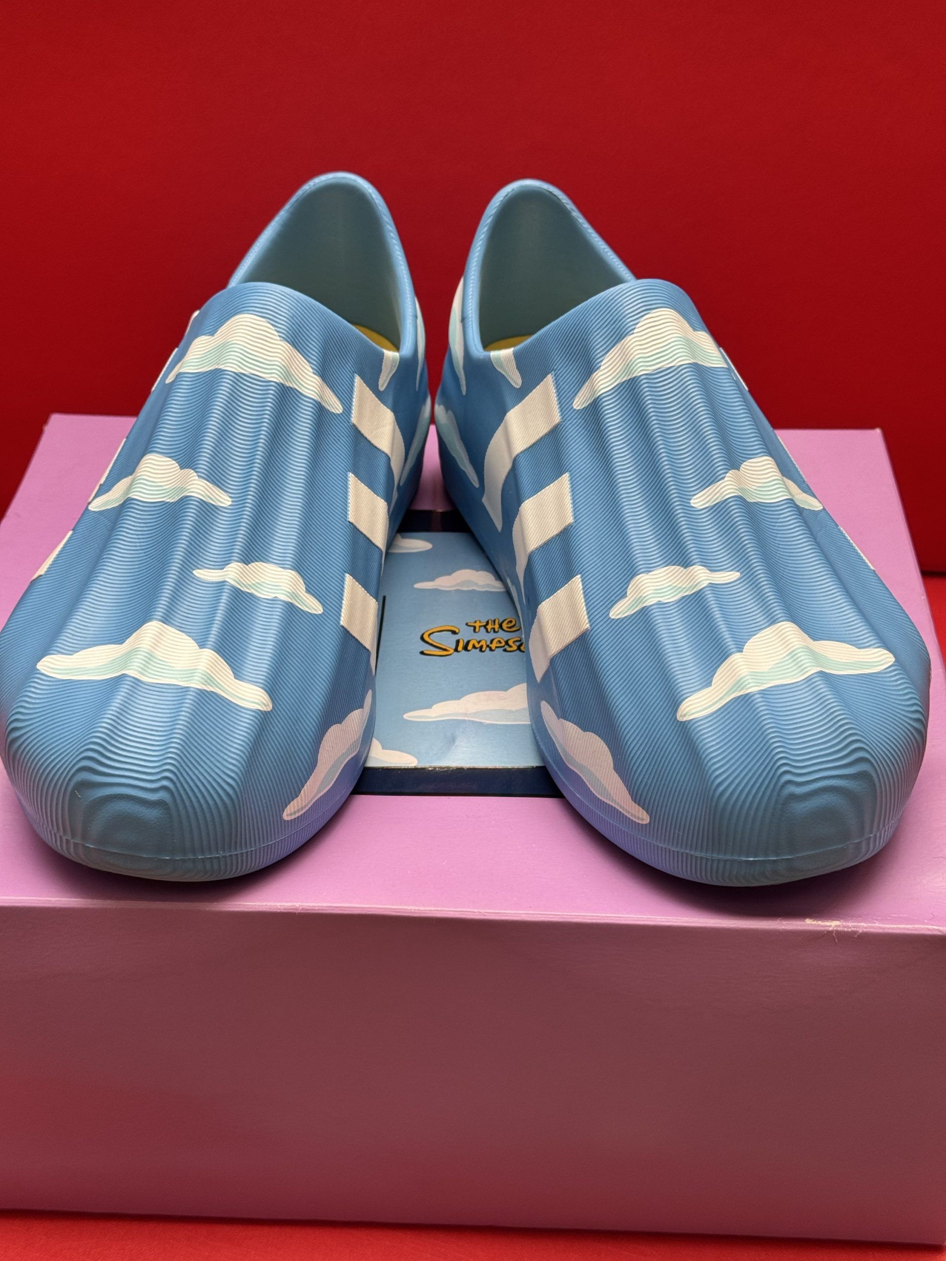 Blue and white cloud-patterned slip-on shoes on a pink box, set against a red background.