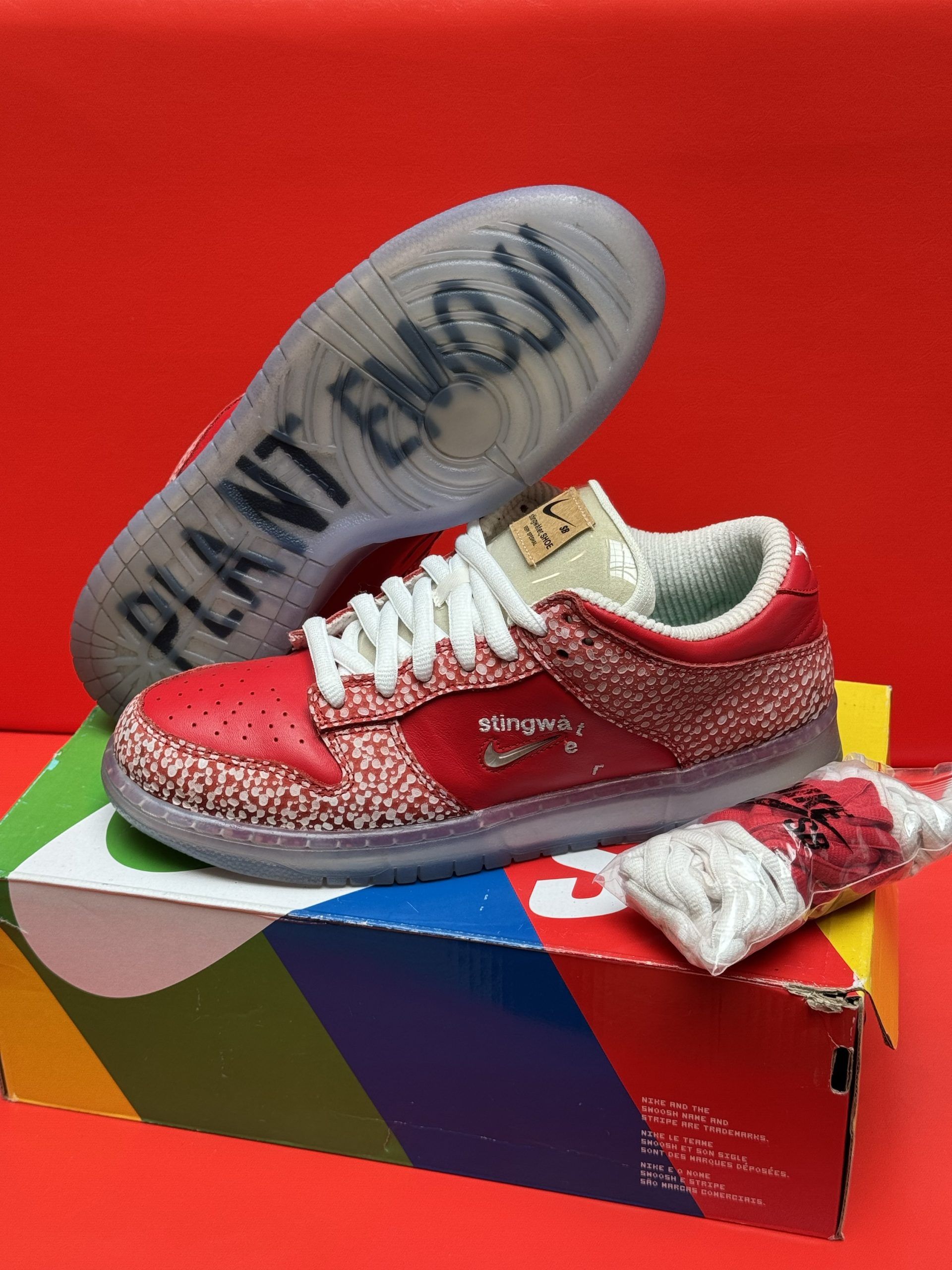 Pair of red speckled Nike Dunks on a colorful shoebox, set against a red background.