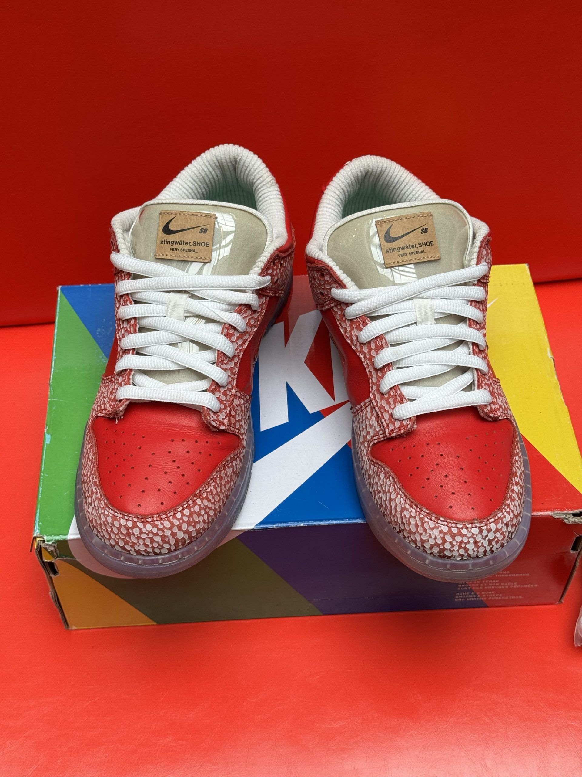 Pair of red speckled Nike Dunks on a colorful shoebox, set against a red background.