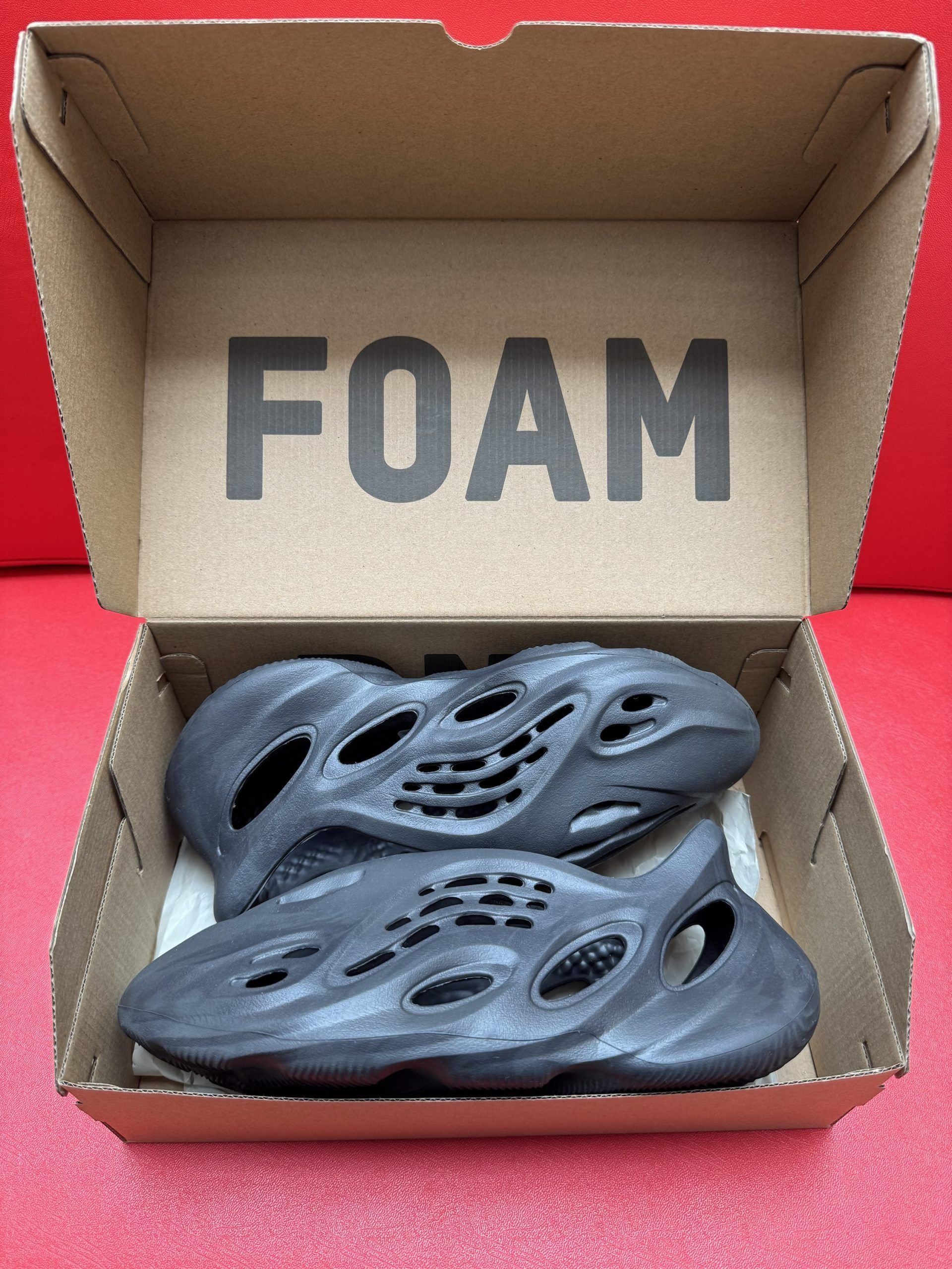 Pair of dark gray Yeezy Foam Runners inside their cardboard box labeled 