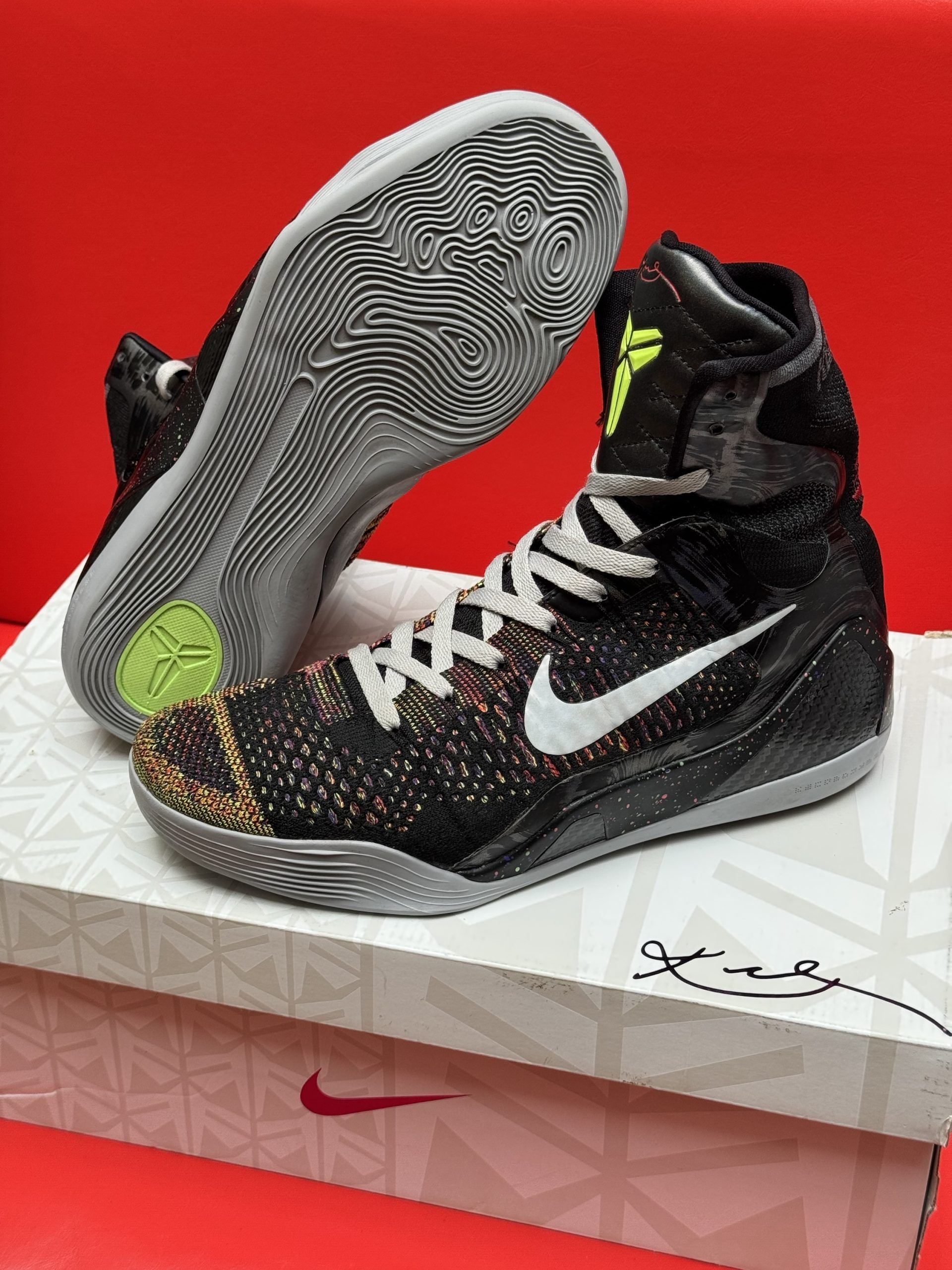 Black and gray Kobe basketball sneakers with white accents, laces, and swoosh logo on a white box.