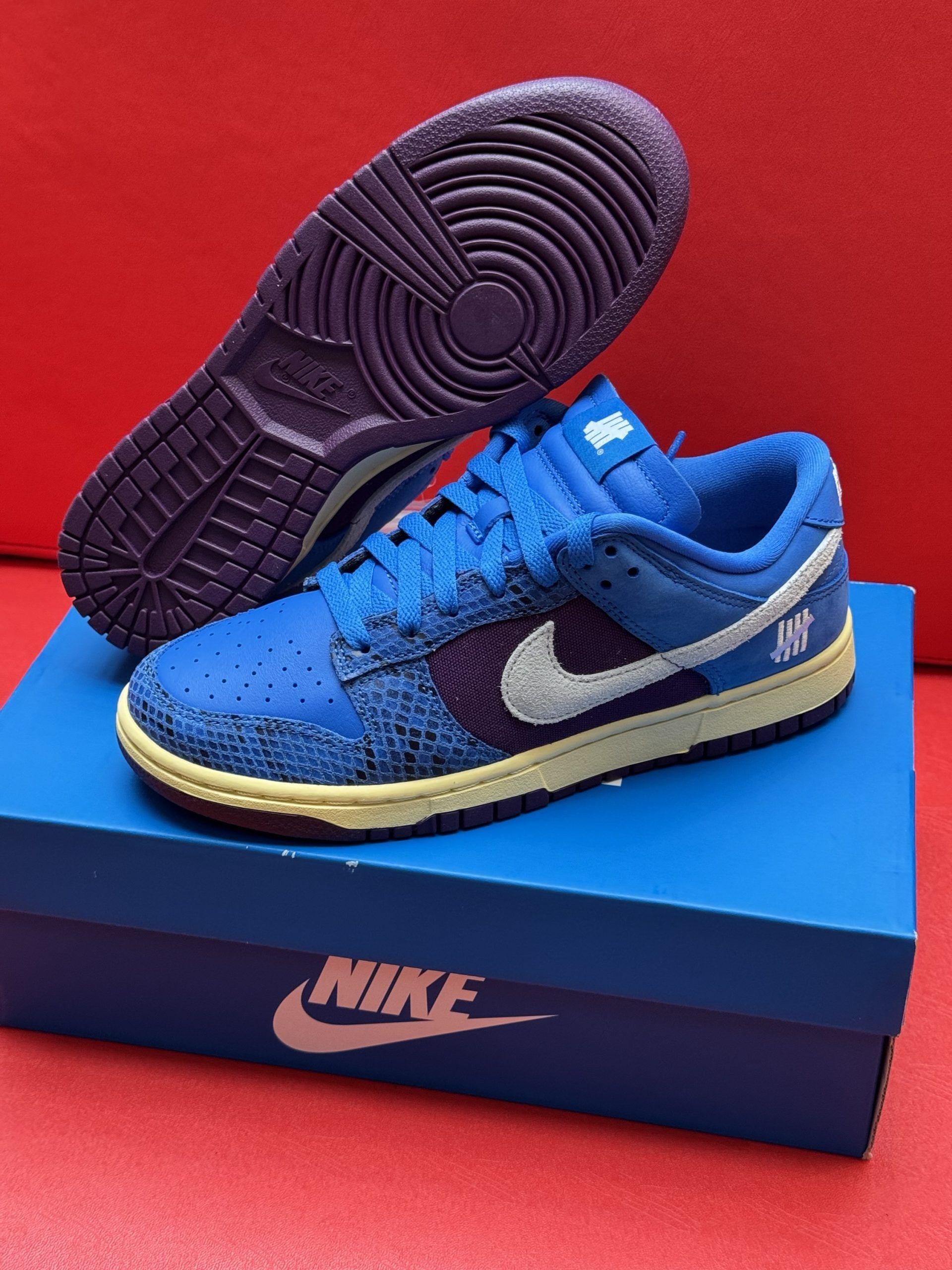 Blue Nike Dunk Low sneakers with purple accents, white swoosh, and purple sole on a blue Nike box.
