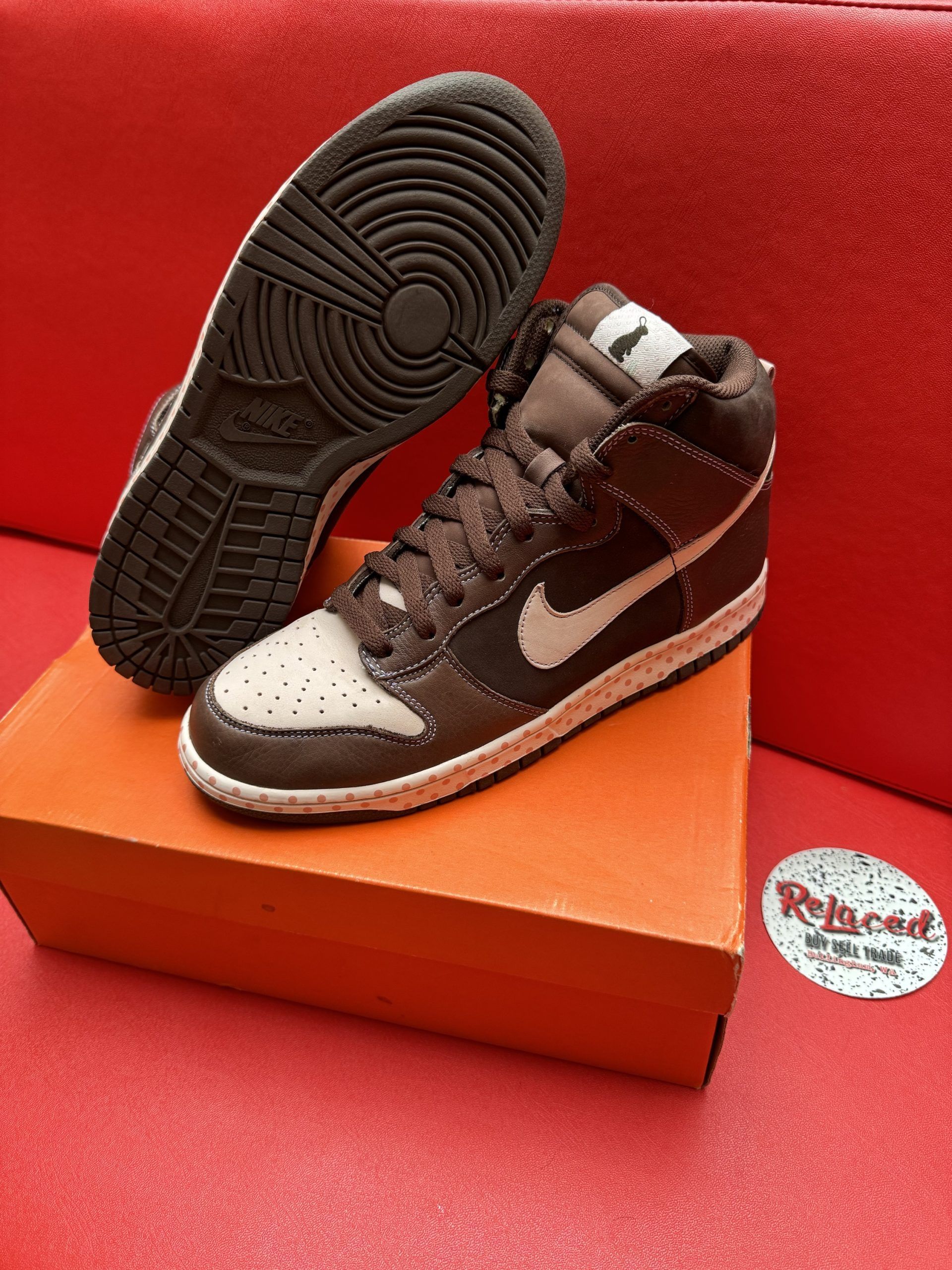 Nike Dunk High sneakers, brown and cream, on an orange box, brown sole, white swoosh on a red surface.