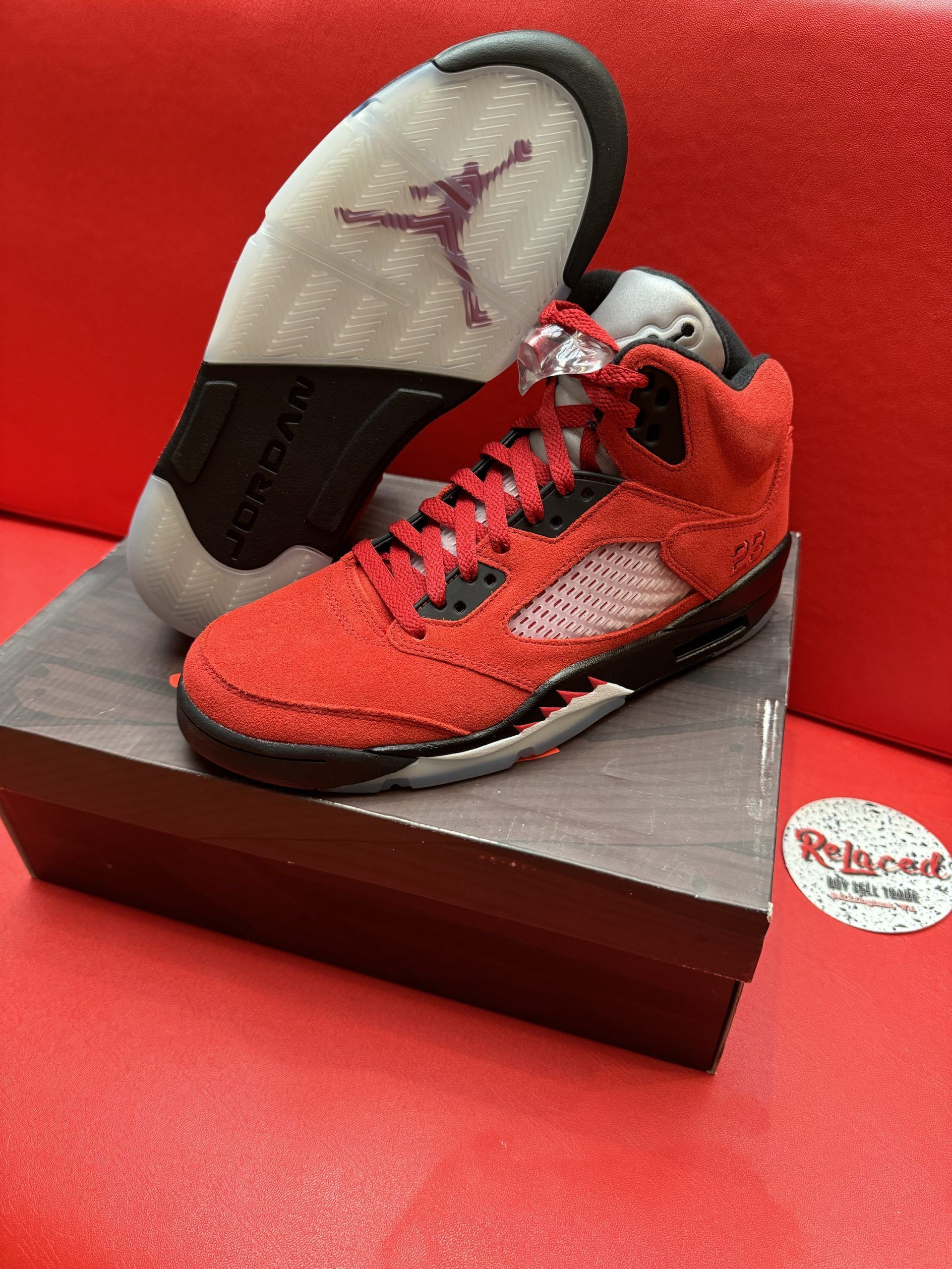 Red and black Jordan 5 sneakers with translucent sole on a box.