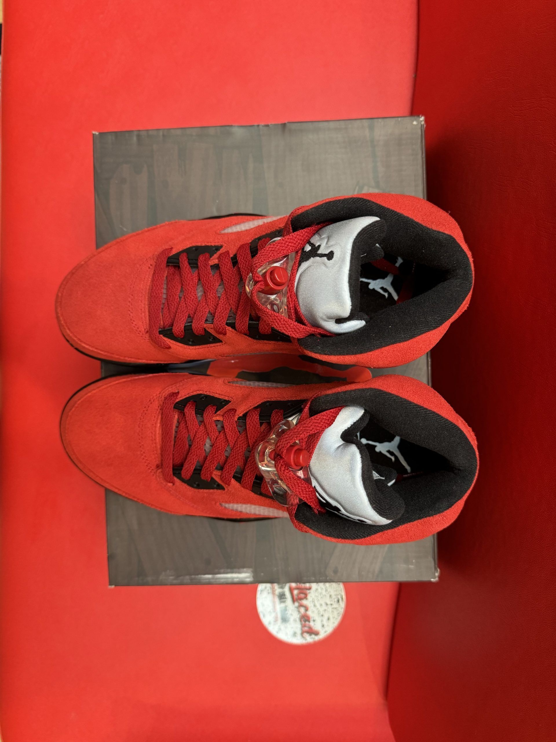 Red and black Jordan 5 sneakers with translucent sole on a box.