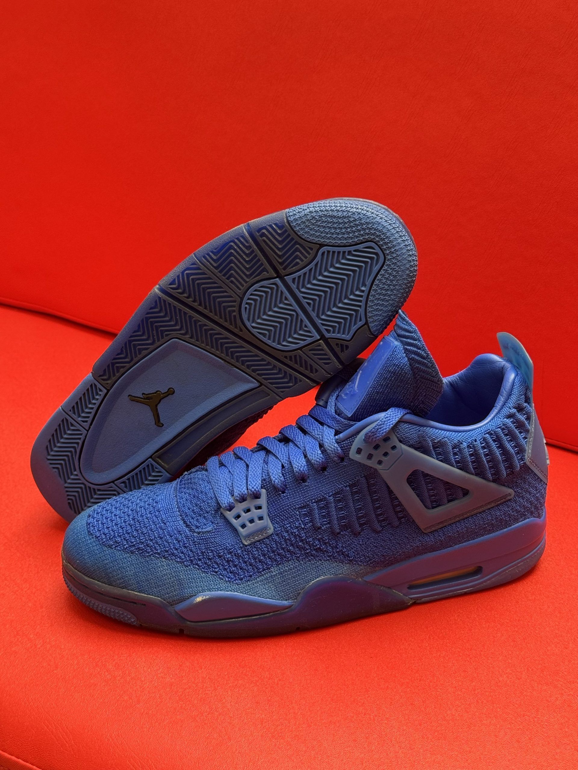 Blue Air Jordan 4 sneakers on a red surface, showcasing textured uppers and soles.