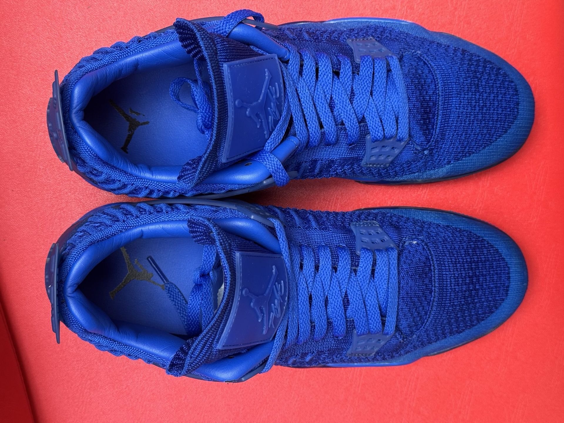 Blue Air Jordan 4 sneakers on a red surface, showcasing textured uppers and soles.