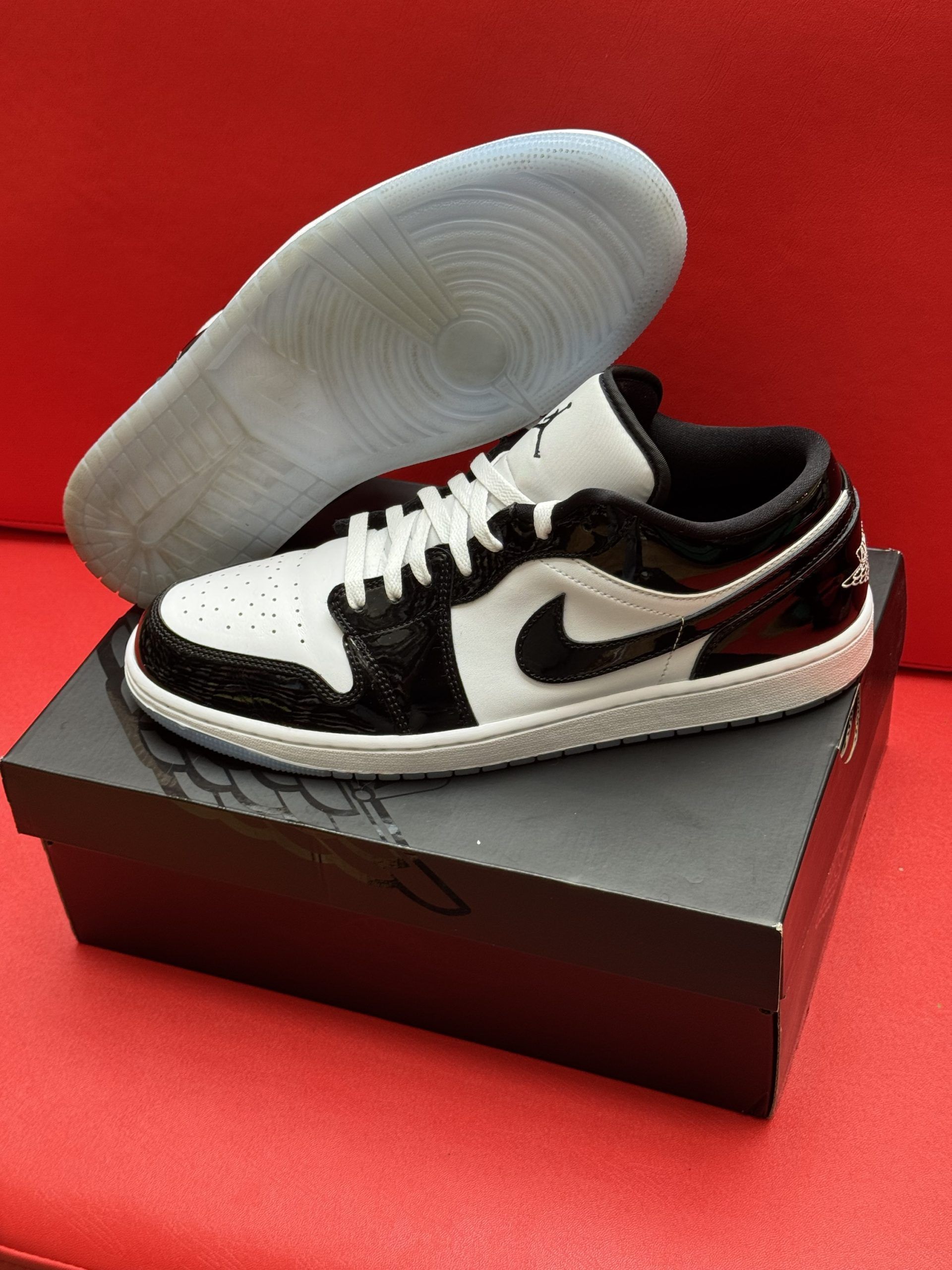 Black and white Air Jordan 1 Low sneaker on a black shoebox with the insole beside it, set against a red background.