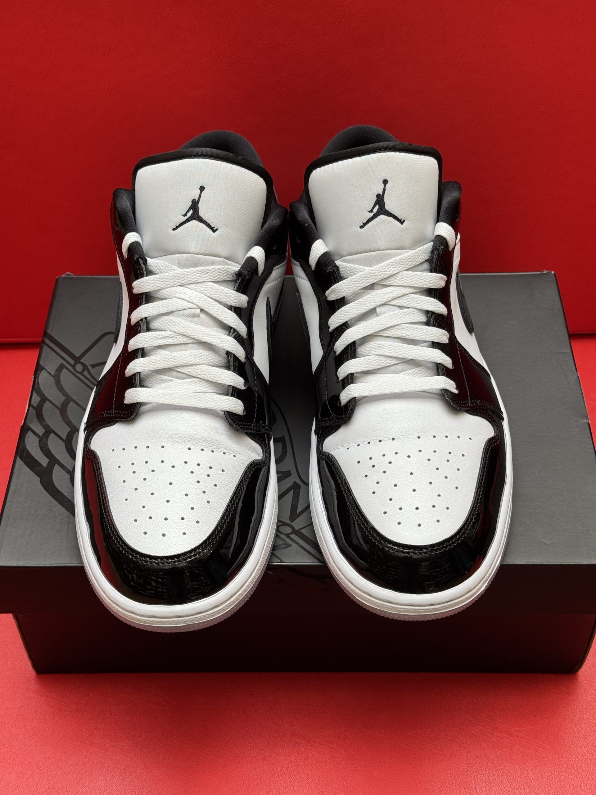 Black and white Air Jordan 1 Low sneaker on a black shoebox with the insole beside it, set against a red background.