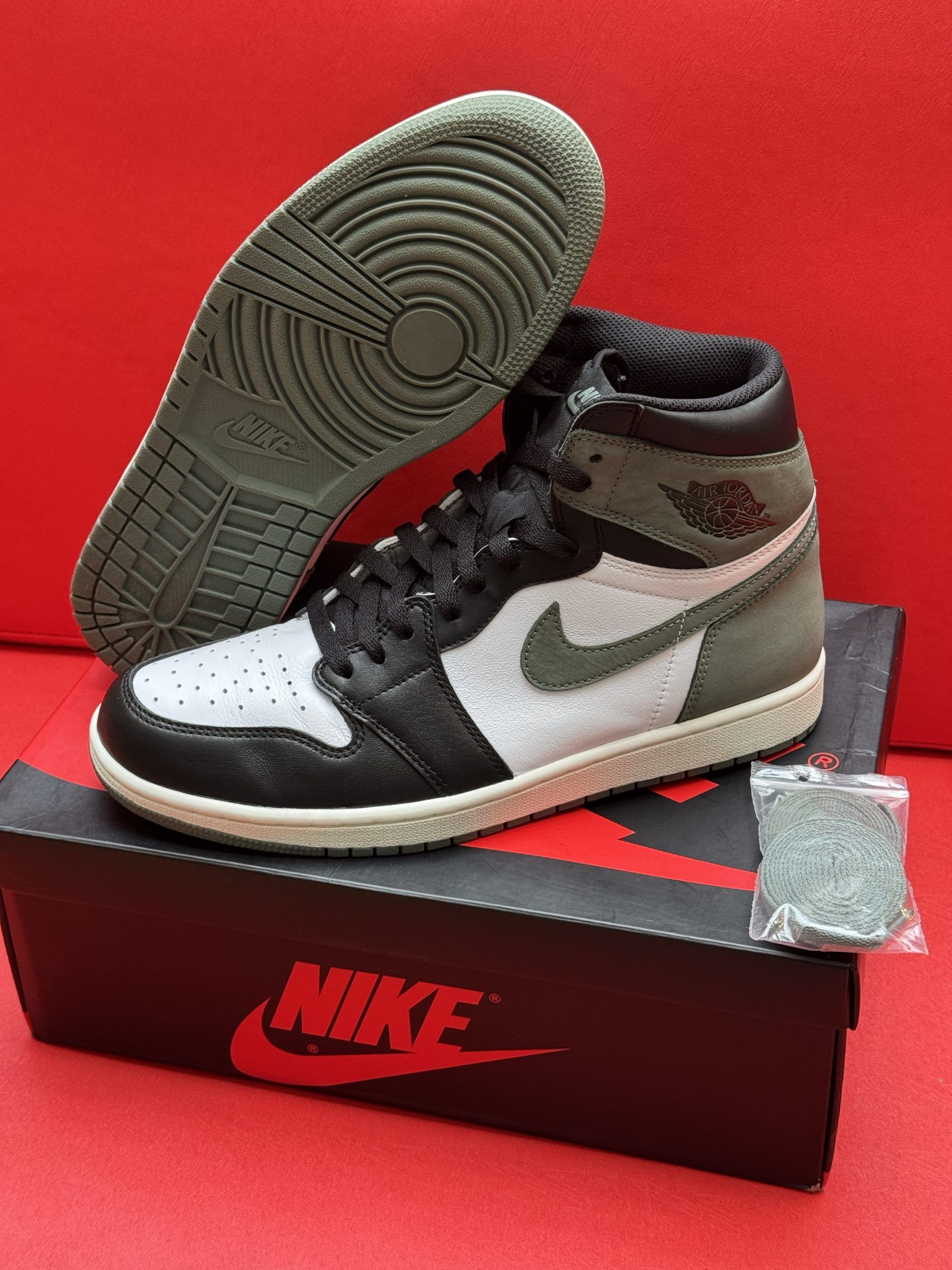 Air Jordan 1 sneaker with black, green, and white color scheme, on box, with extra laces and sole visible.