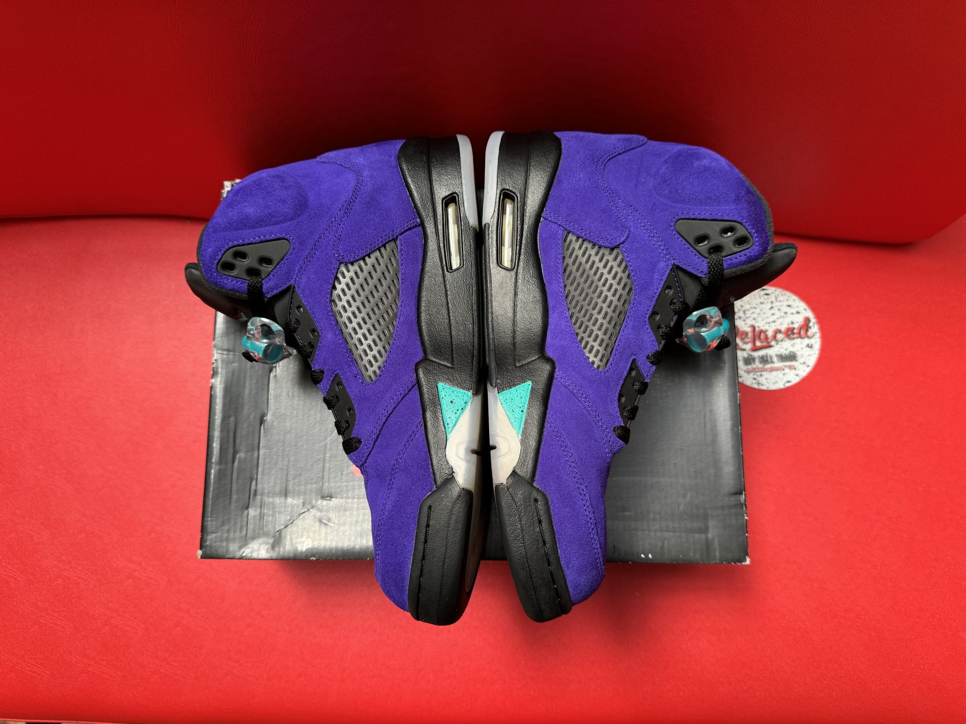 Purple and black Air Jordan 5 sneakers on a box, sole up, with a red background.