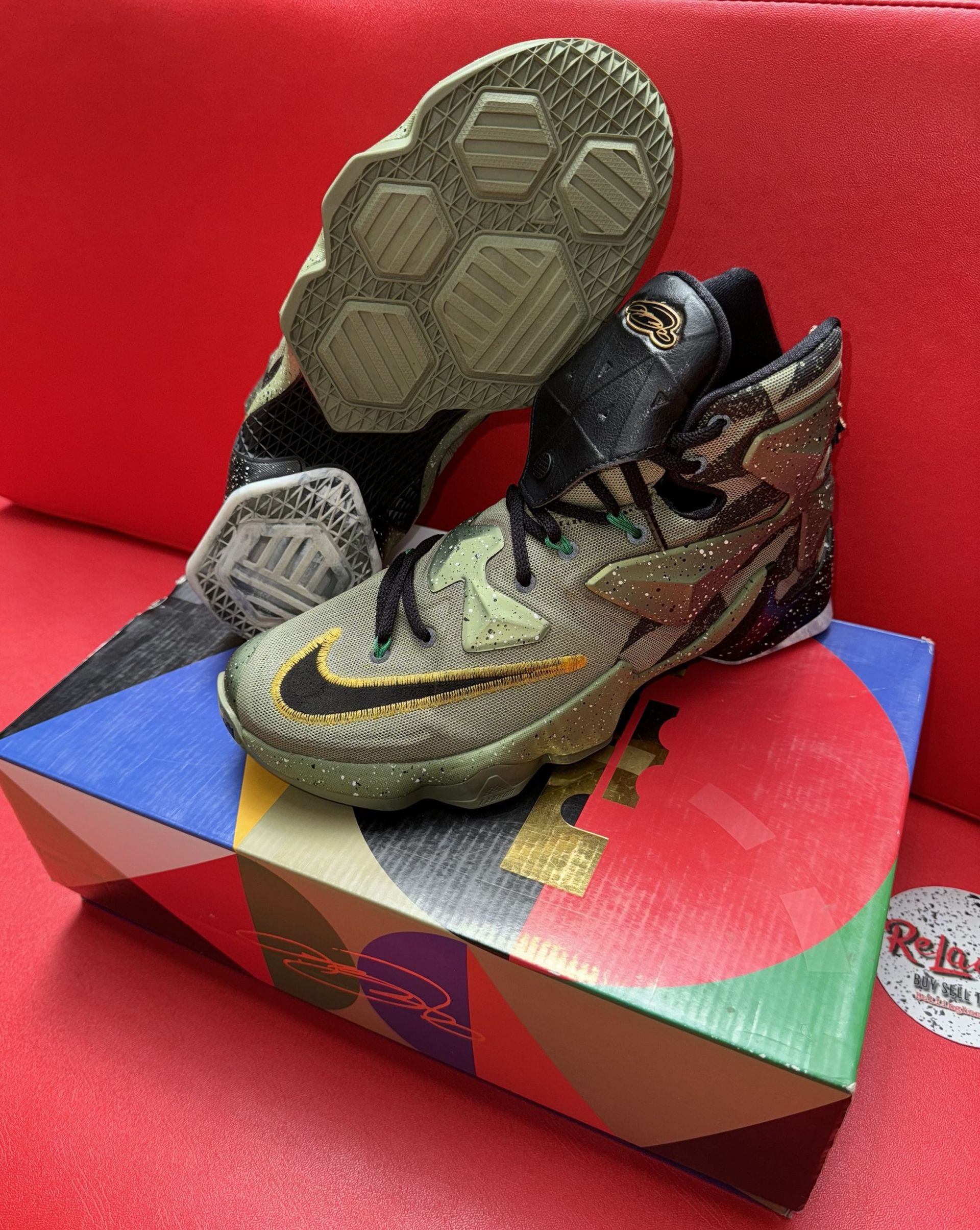 Camouflage Nike LeBron basketball sneakers on a colorful patterned box, red background.