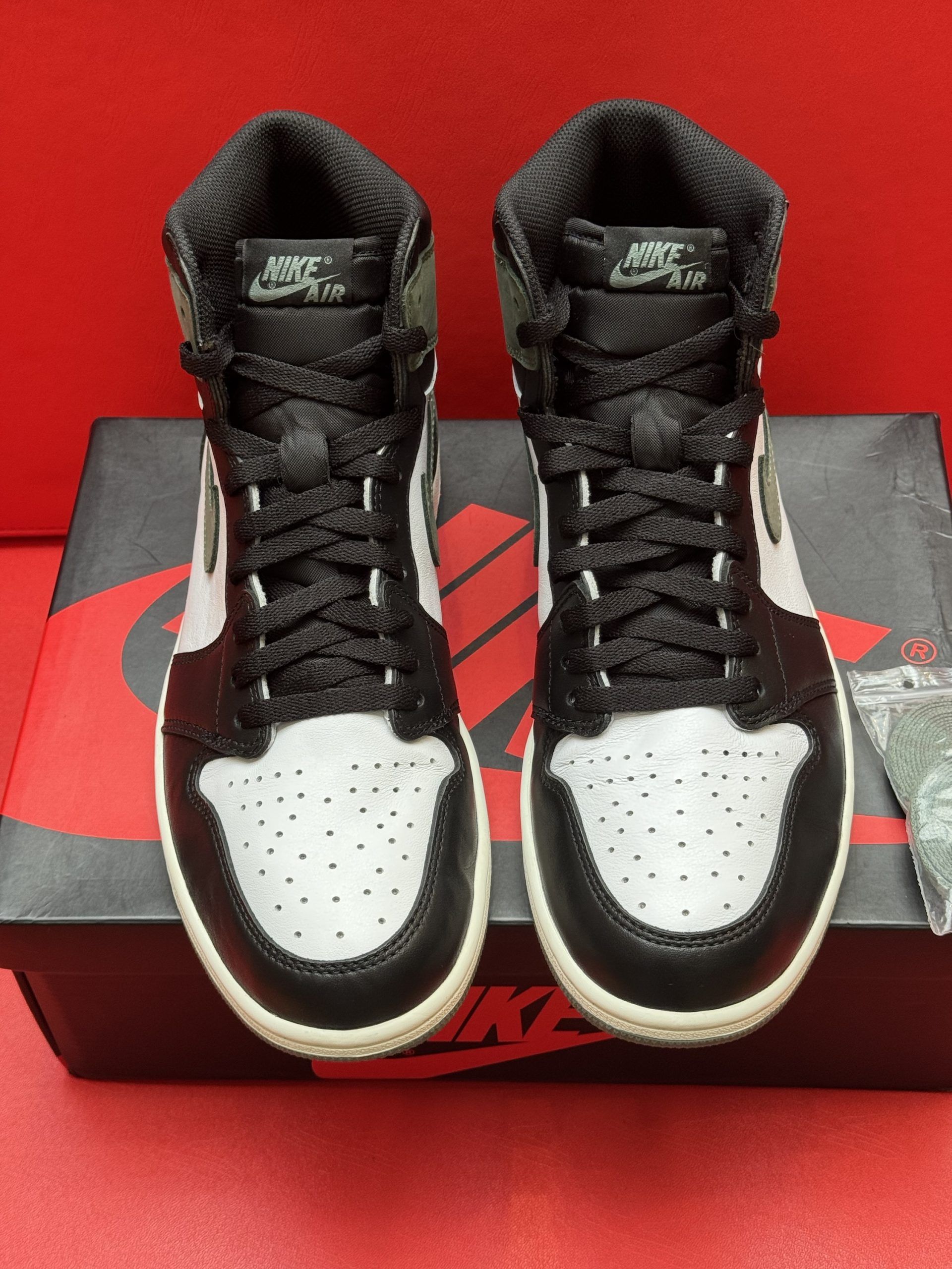 Air Jordan 1 sneaker with black, green, and white color scheme, on box, with extra laces and sole visible.