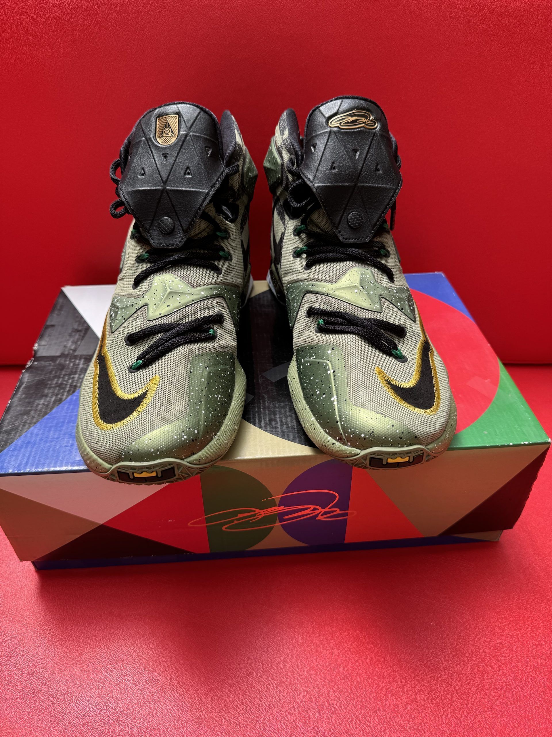 Camouflage Nike LeBron basketball sneakers on a colorful patterned box, red background.