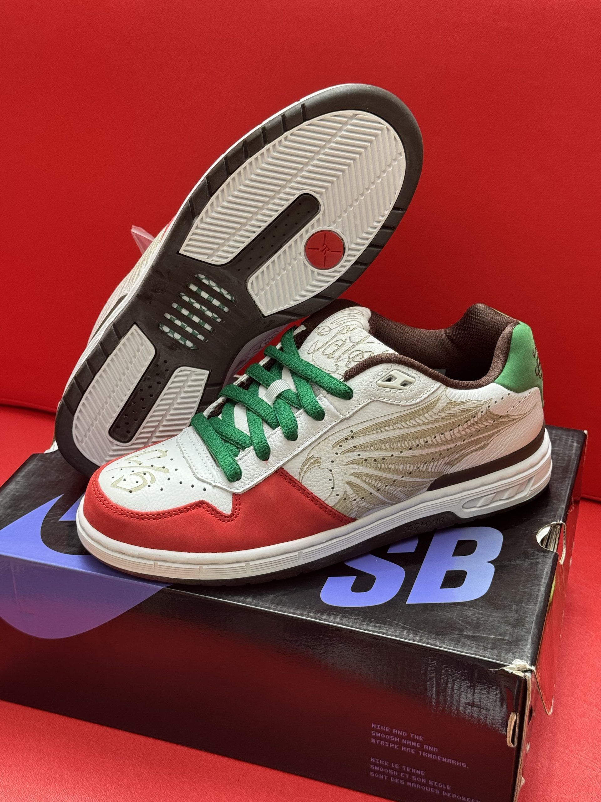 Pair of Nike SB sneakers on a box. White, red, green, and brown colors. Underside of shoe visible.