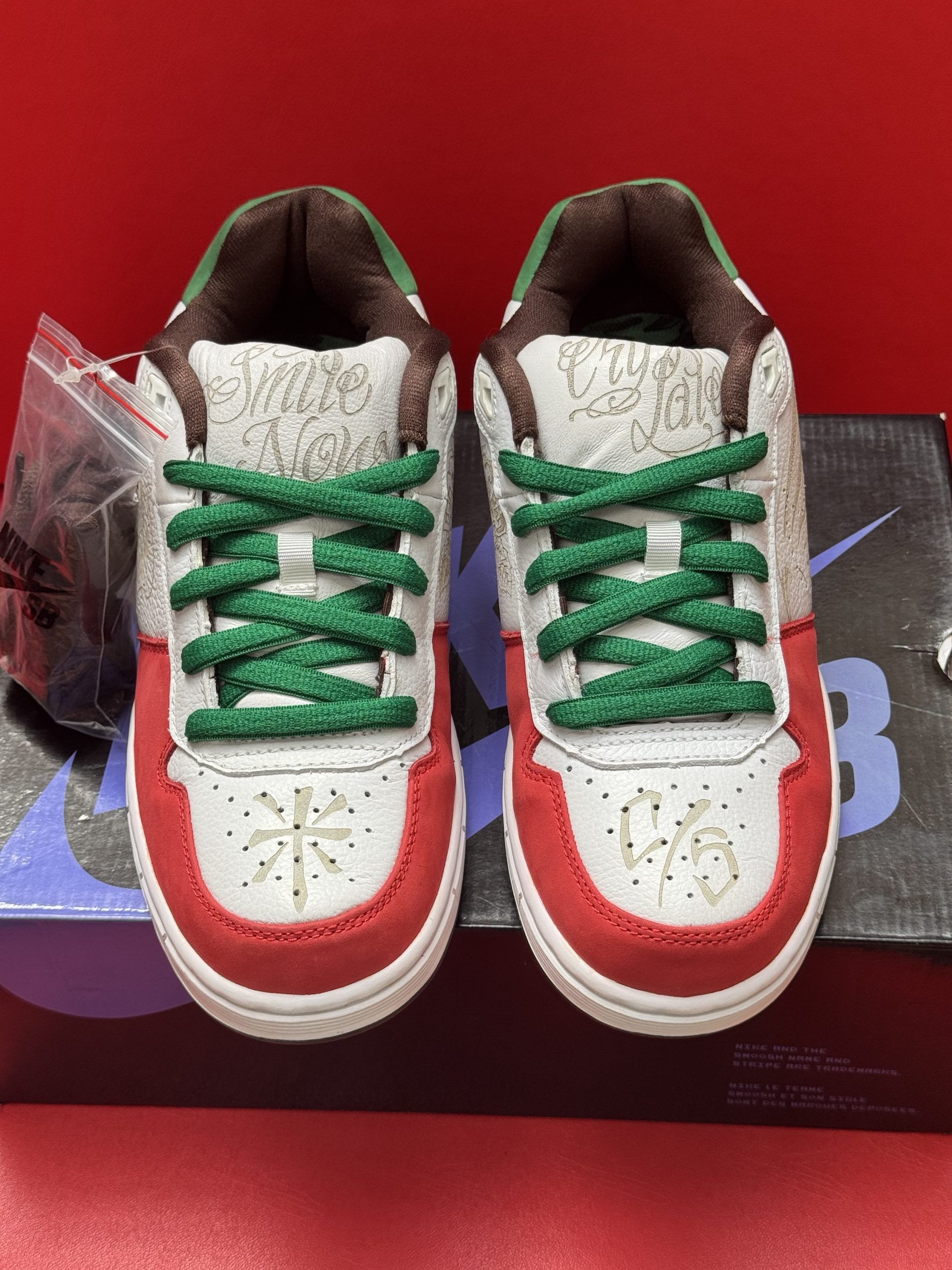 Pair of Nike SB sneakers on a box. White, red, green, and brown colors. Underside of shoe visible.