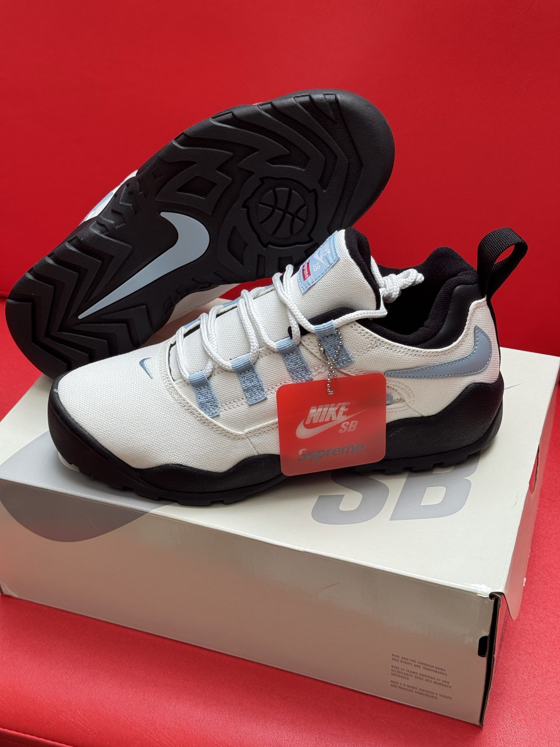 White and light blue Nike SB sneakers on a white box, red tag, black sole, red background.
