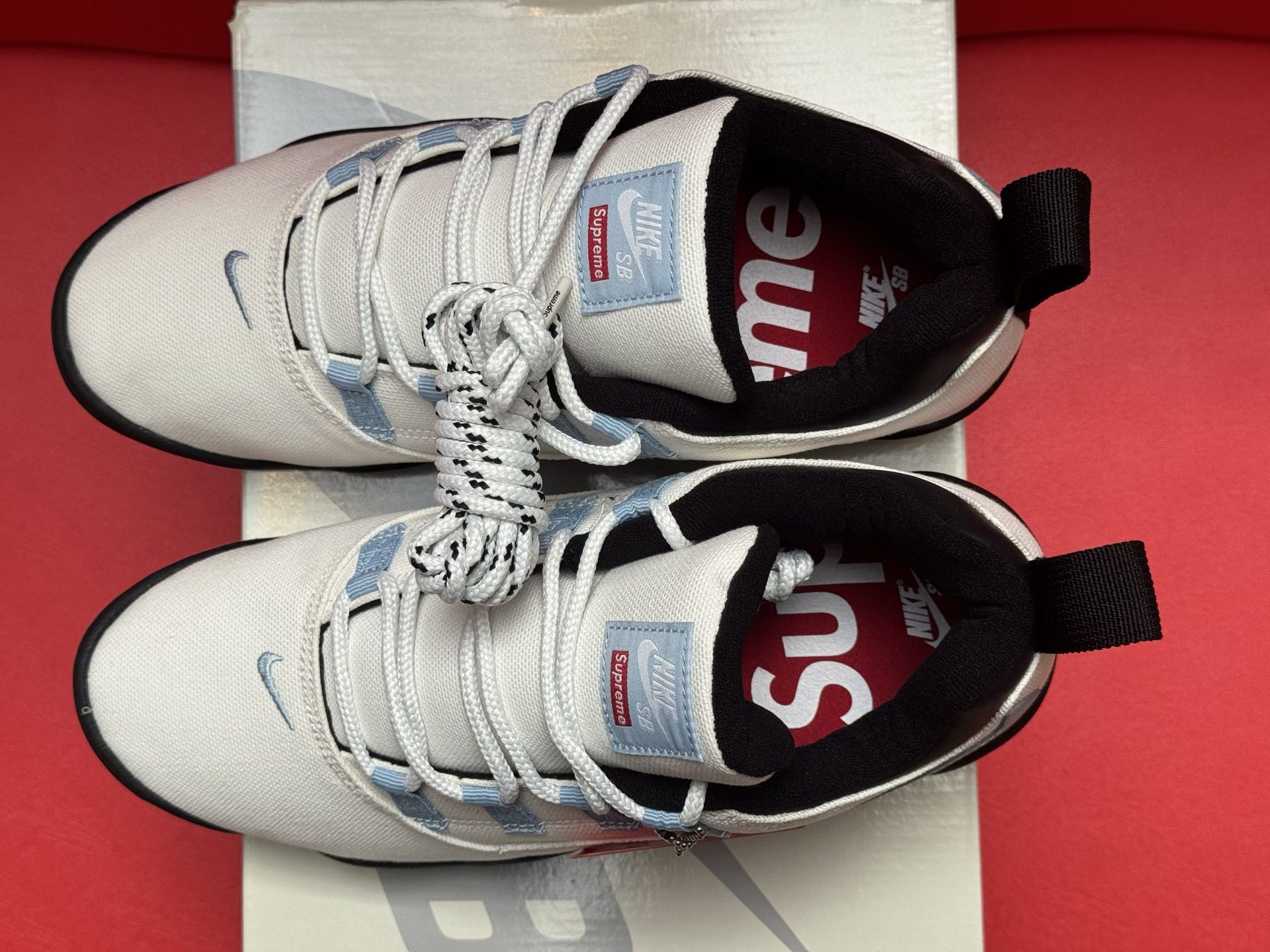 White and light blue Nike SB sneakers on a white box, red tag, black sole, red background.