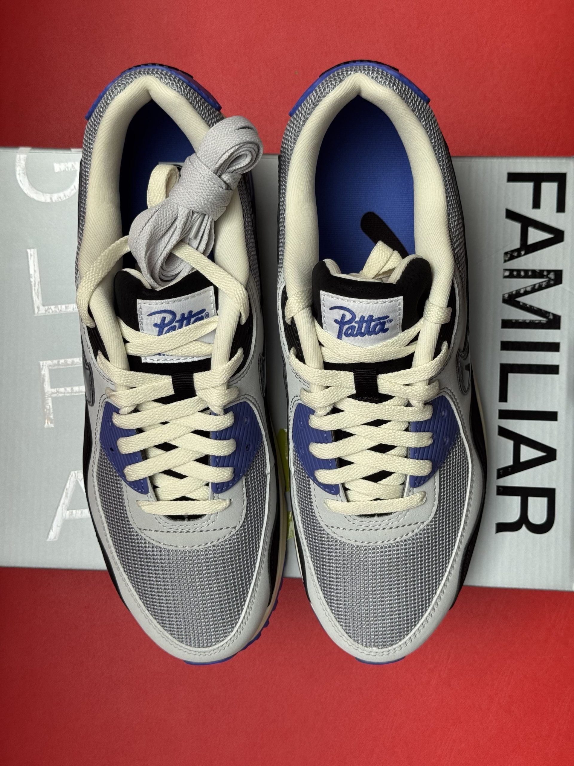 Nike Air Max 90 sneakers, black and blue, on a Patta box, red background.