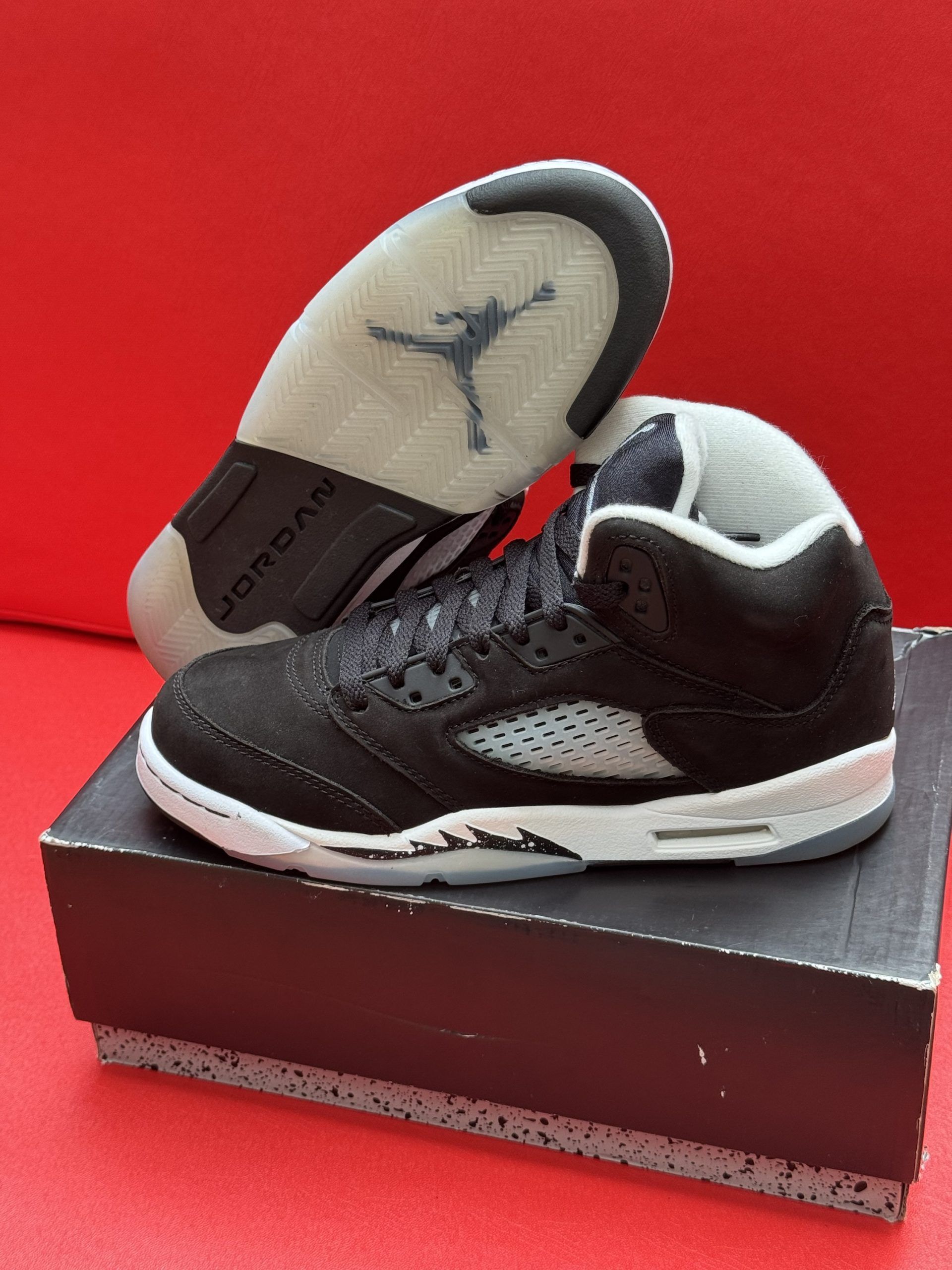 Black and gray Air Jordan 5 sneakers on a black and gray box, red background.
