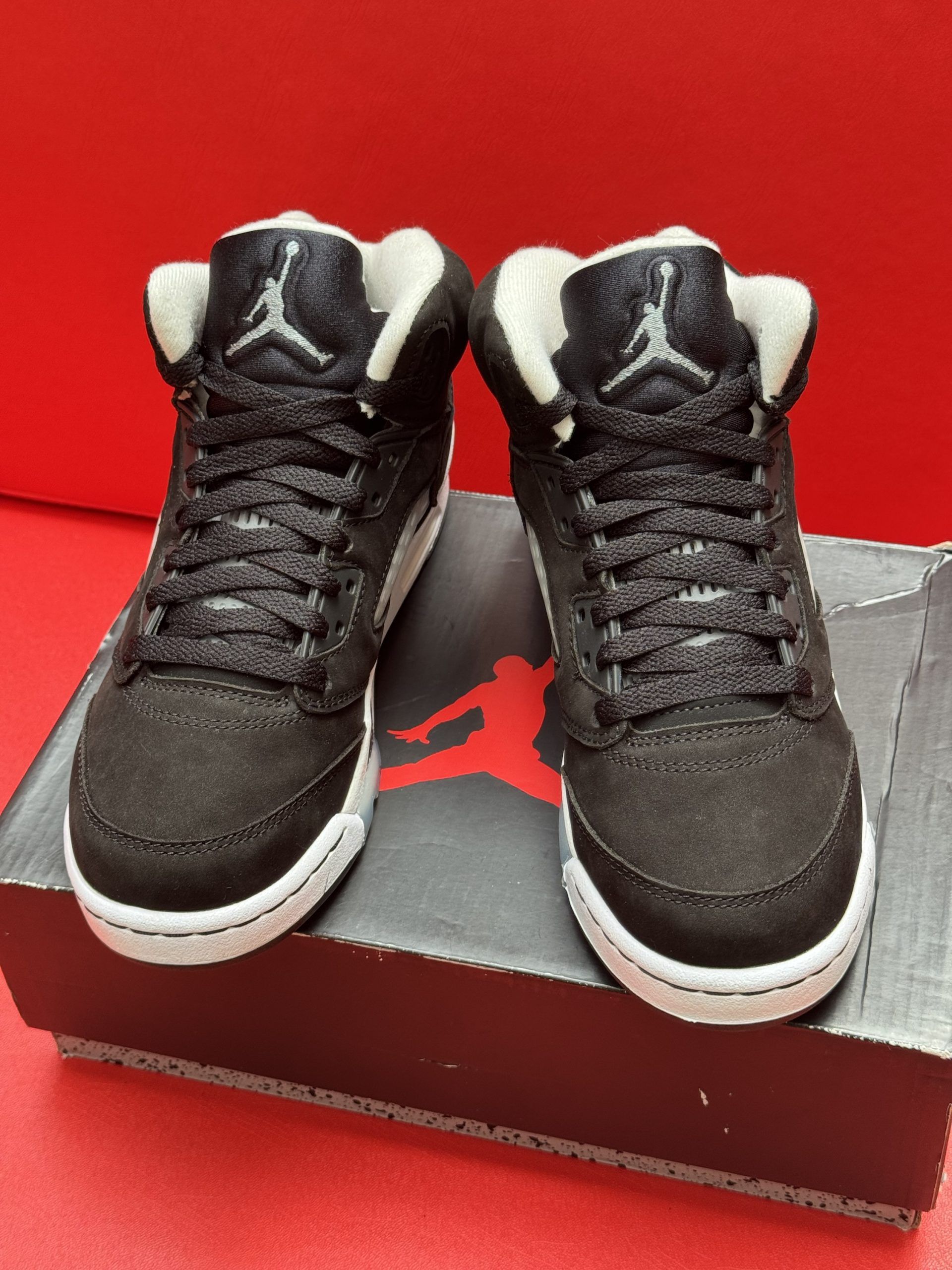 Black and gray Air Jordan 5 sneakers on a black and gray box, red background.