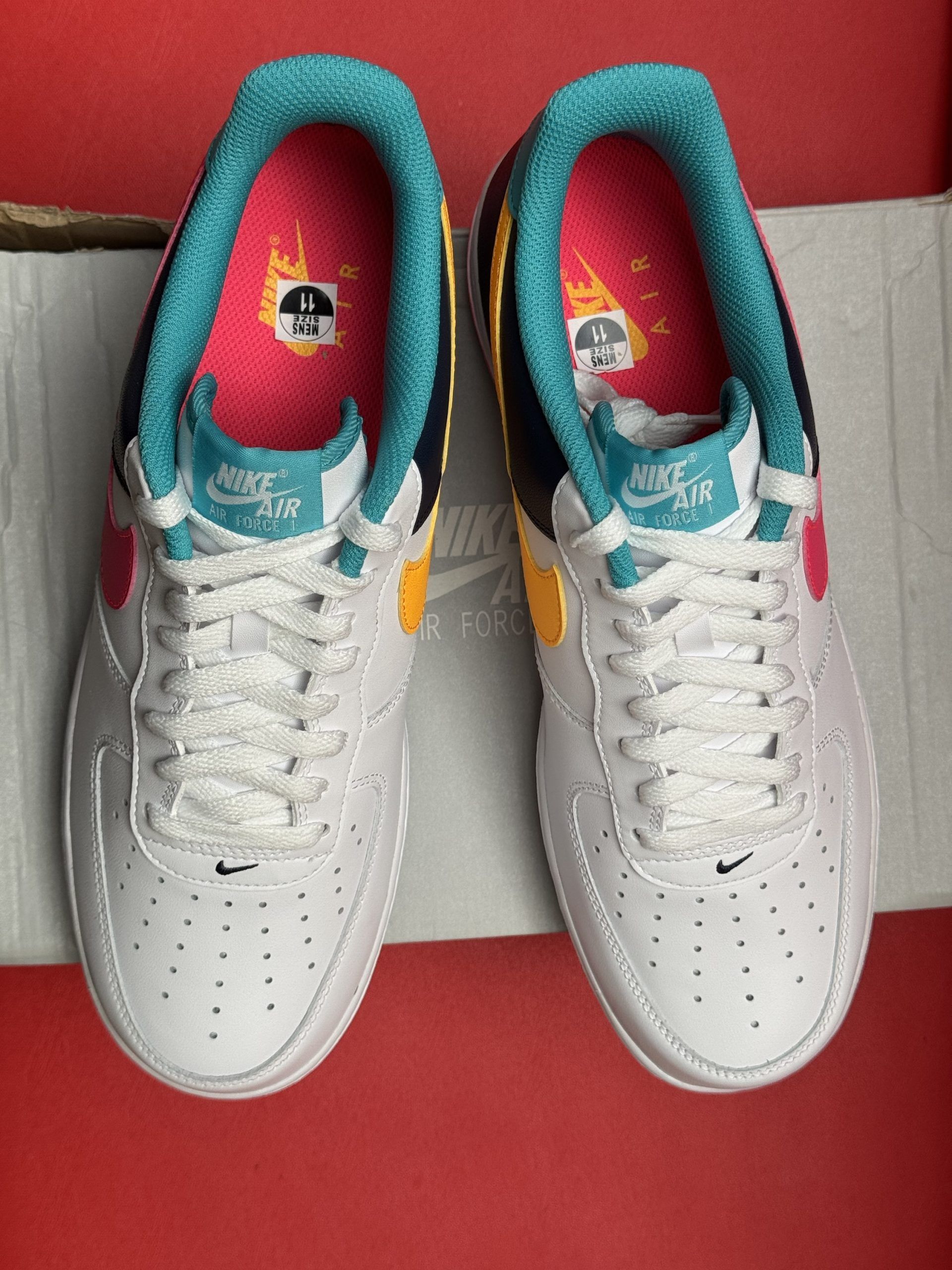 White Nike Air Force 1 sneaker with pink and teal accents, displayed on a shoebox.