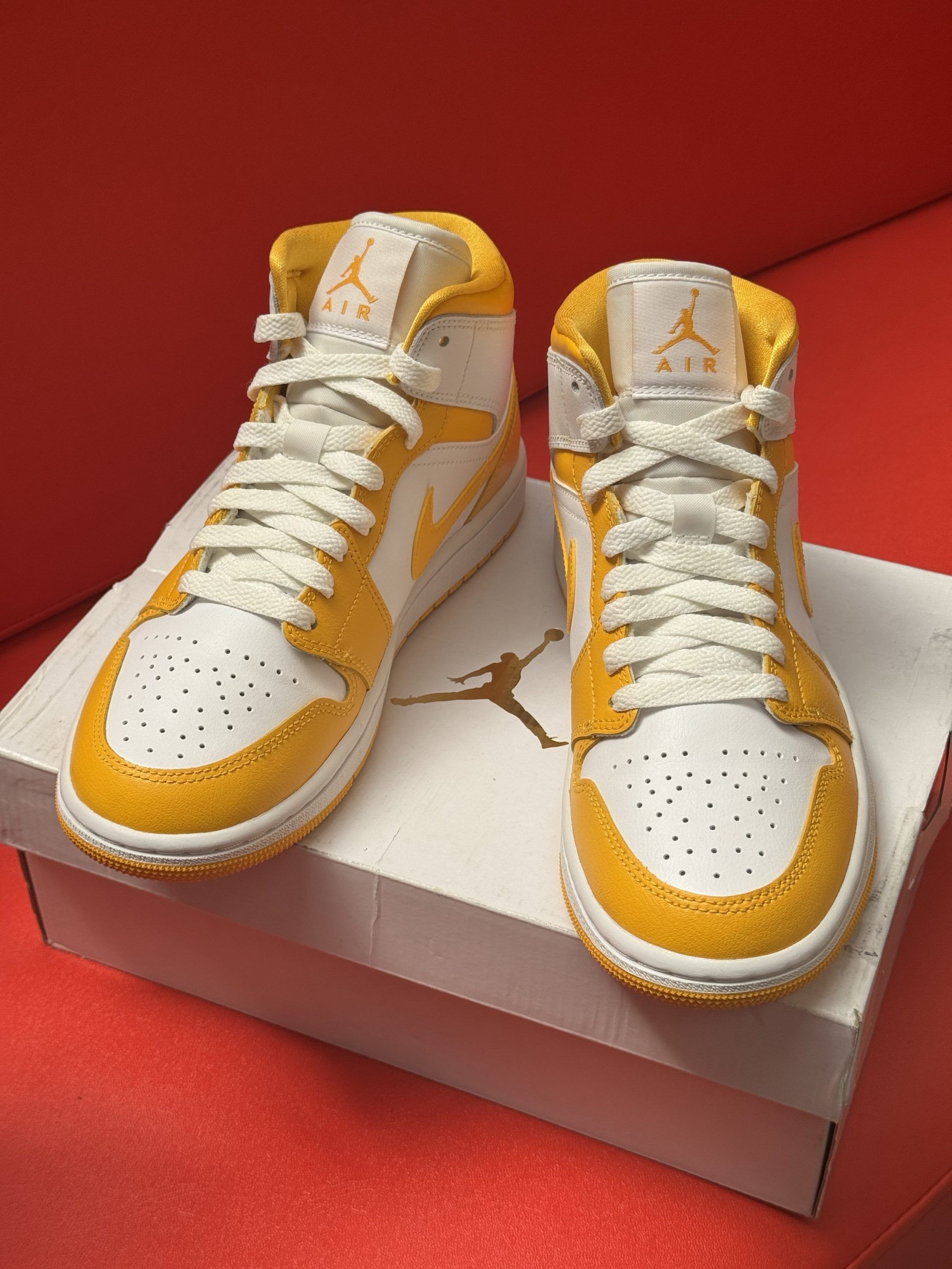 Yellow and white Air Jordan Mid sneaker on a box, with a yellow sole visible beside it.