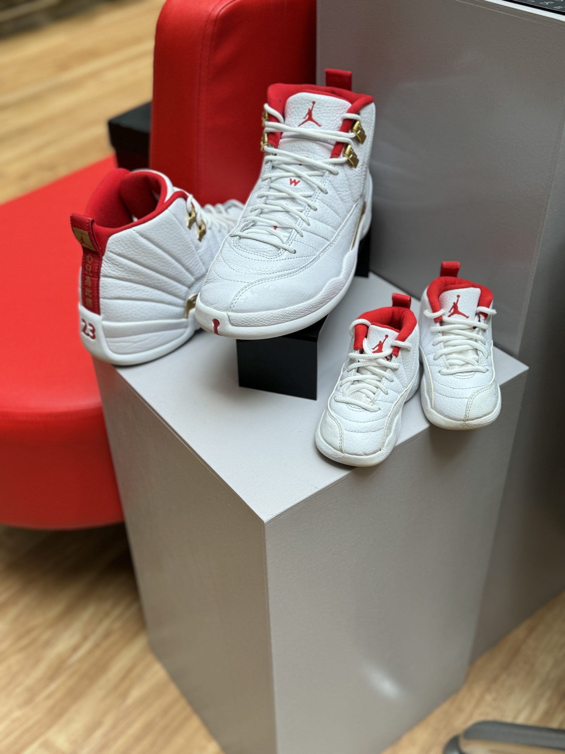 White and red Air Jordan 12 sneakers on a black patterned box, set against a red background.