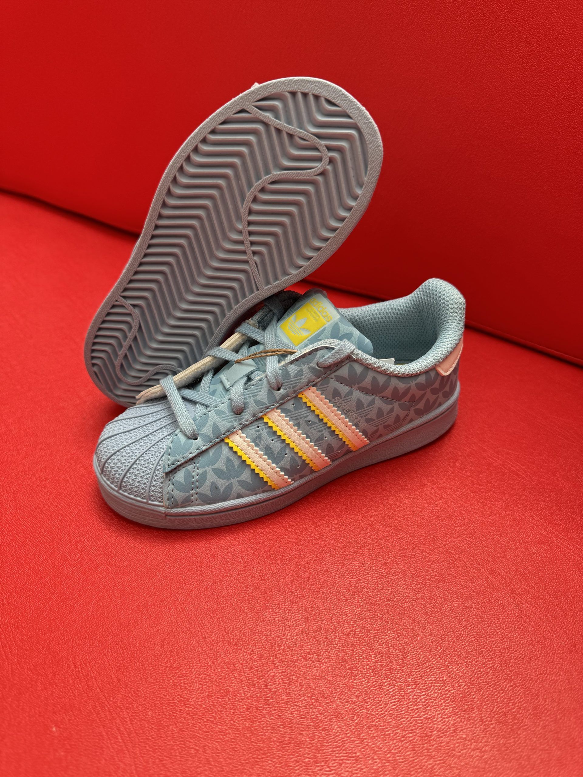 Blue and yellow Adidas Superstar sneakers on a red surface.