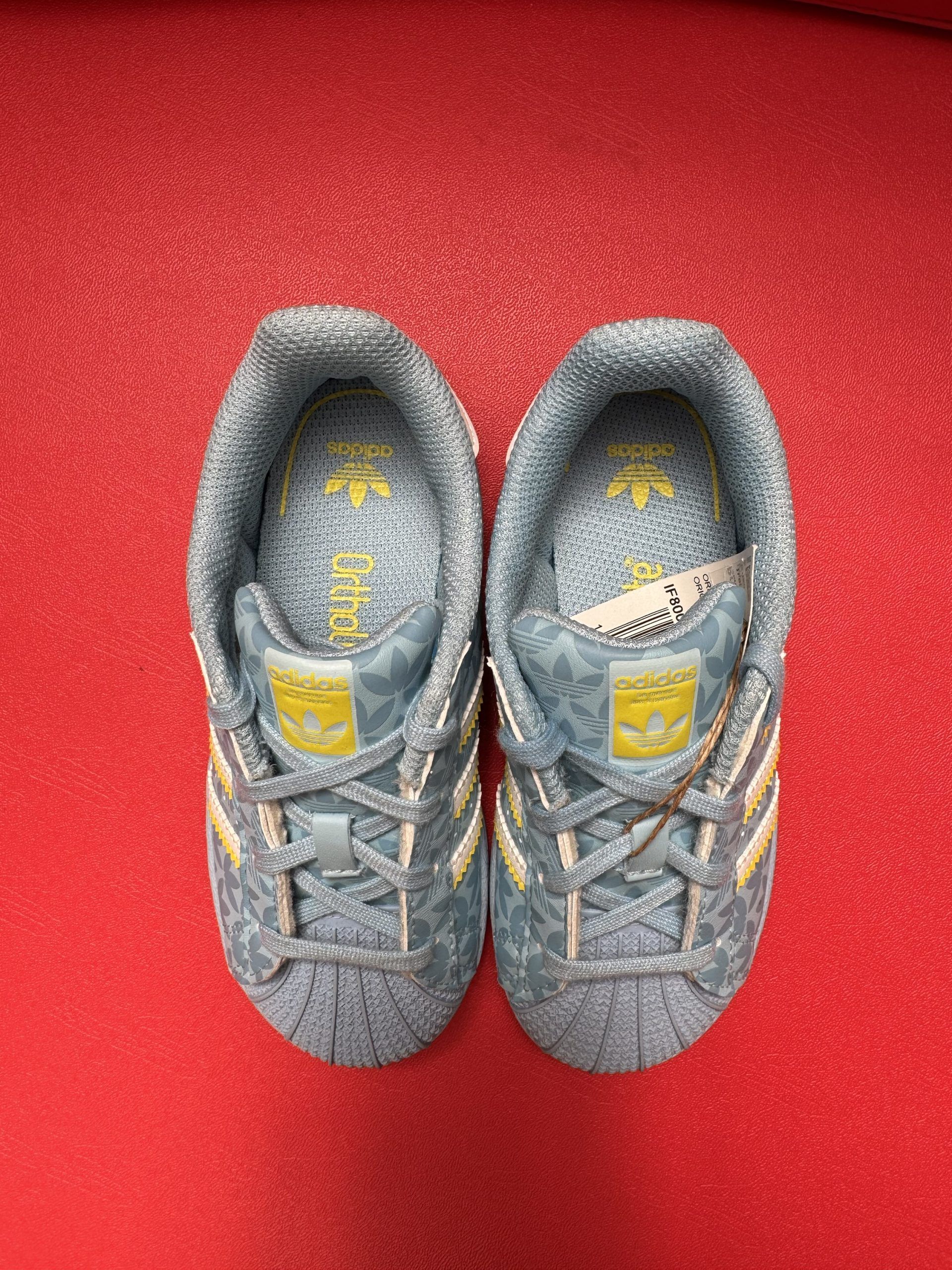 Blue and yellow Adidas Superstar sneakers on a red surface.