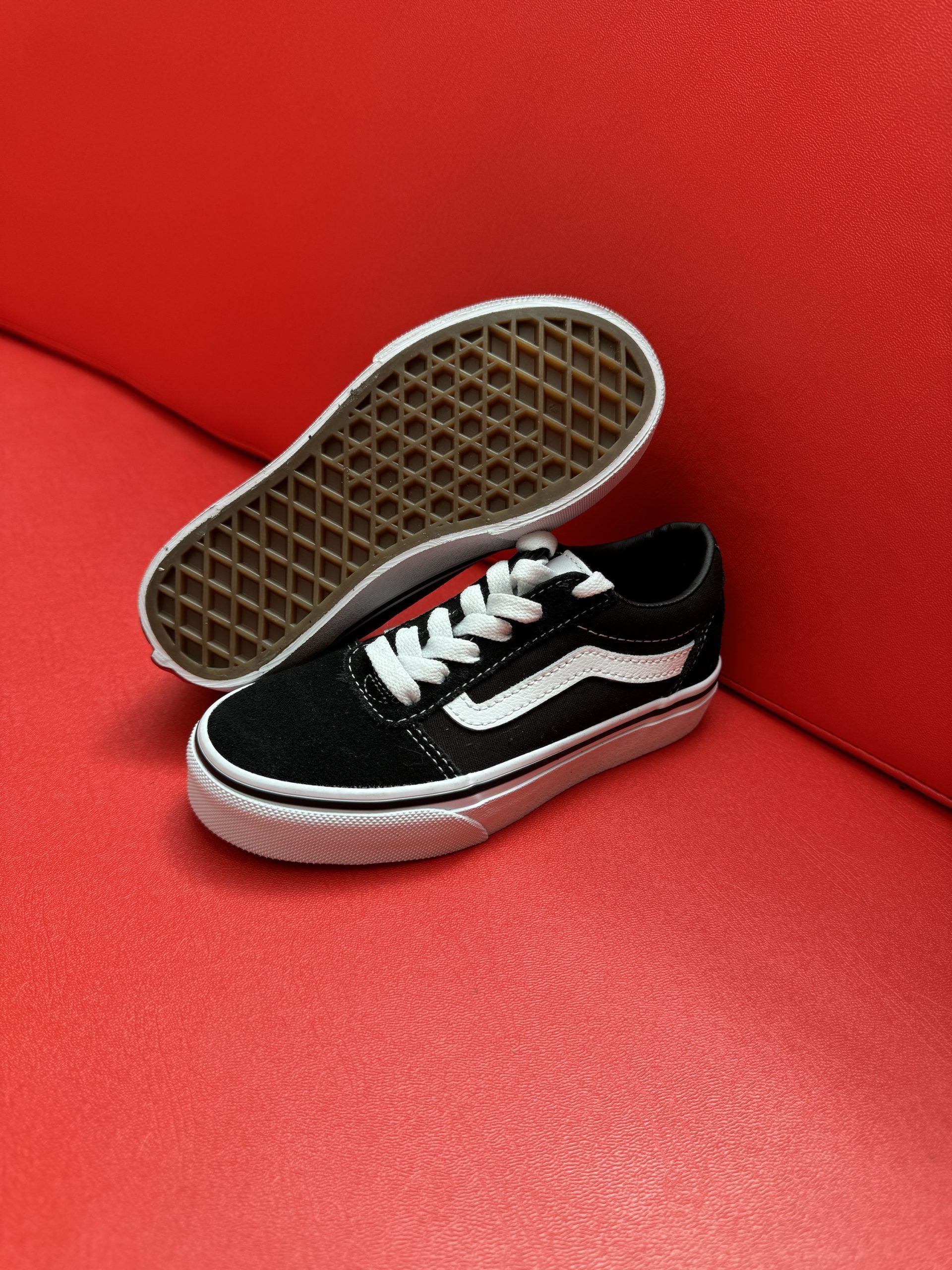 Black and white Vans sneaker on a red surface, with the sole of the other shoe visible.