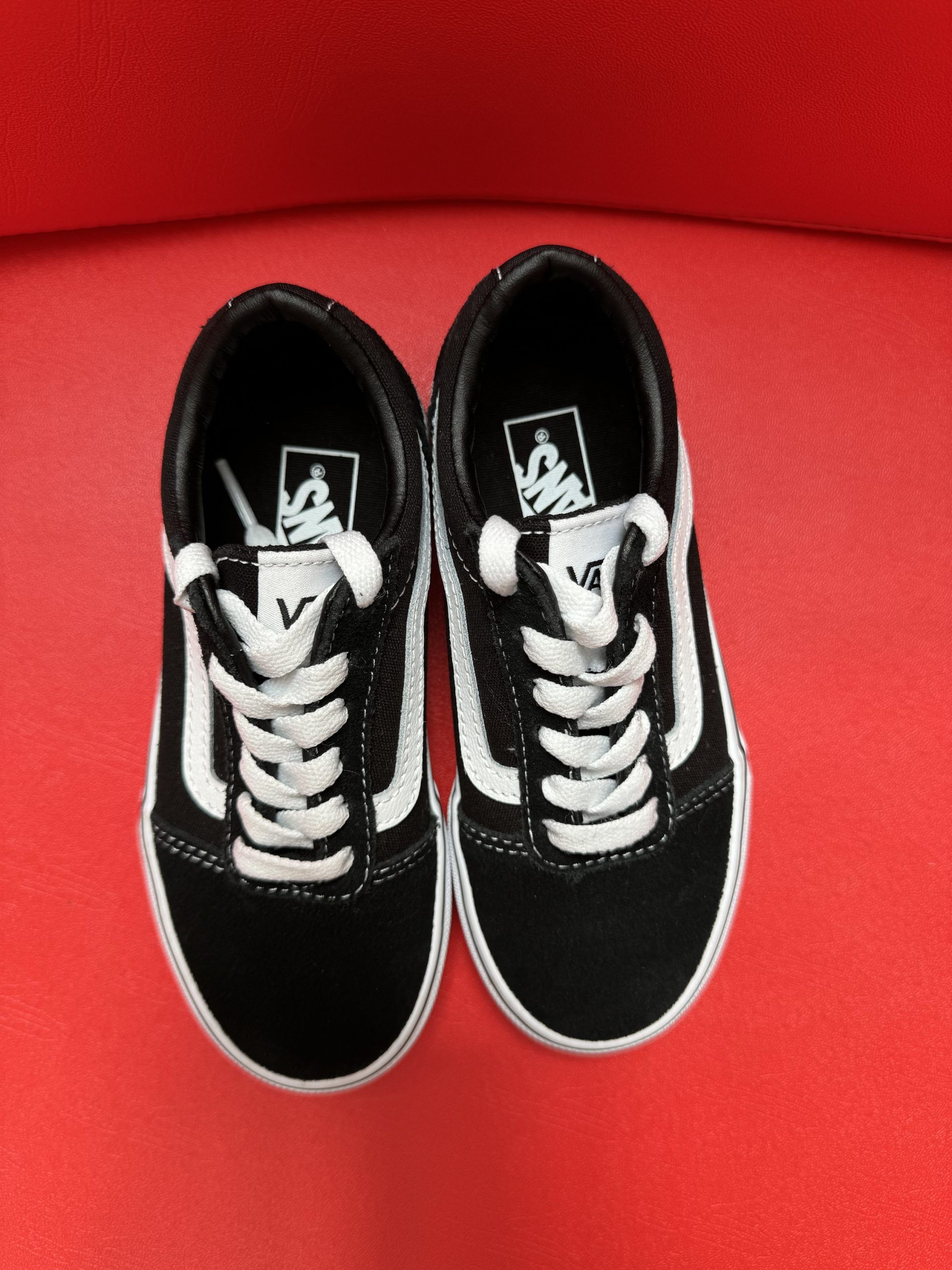 Black and white Vans sneaker on a red surface, with the sole of the other shoe visible.