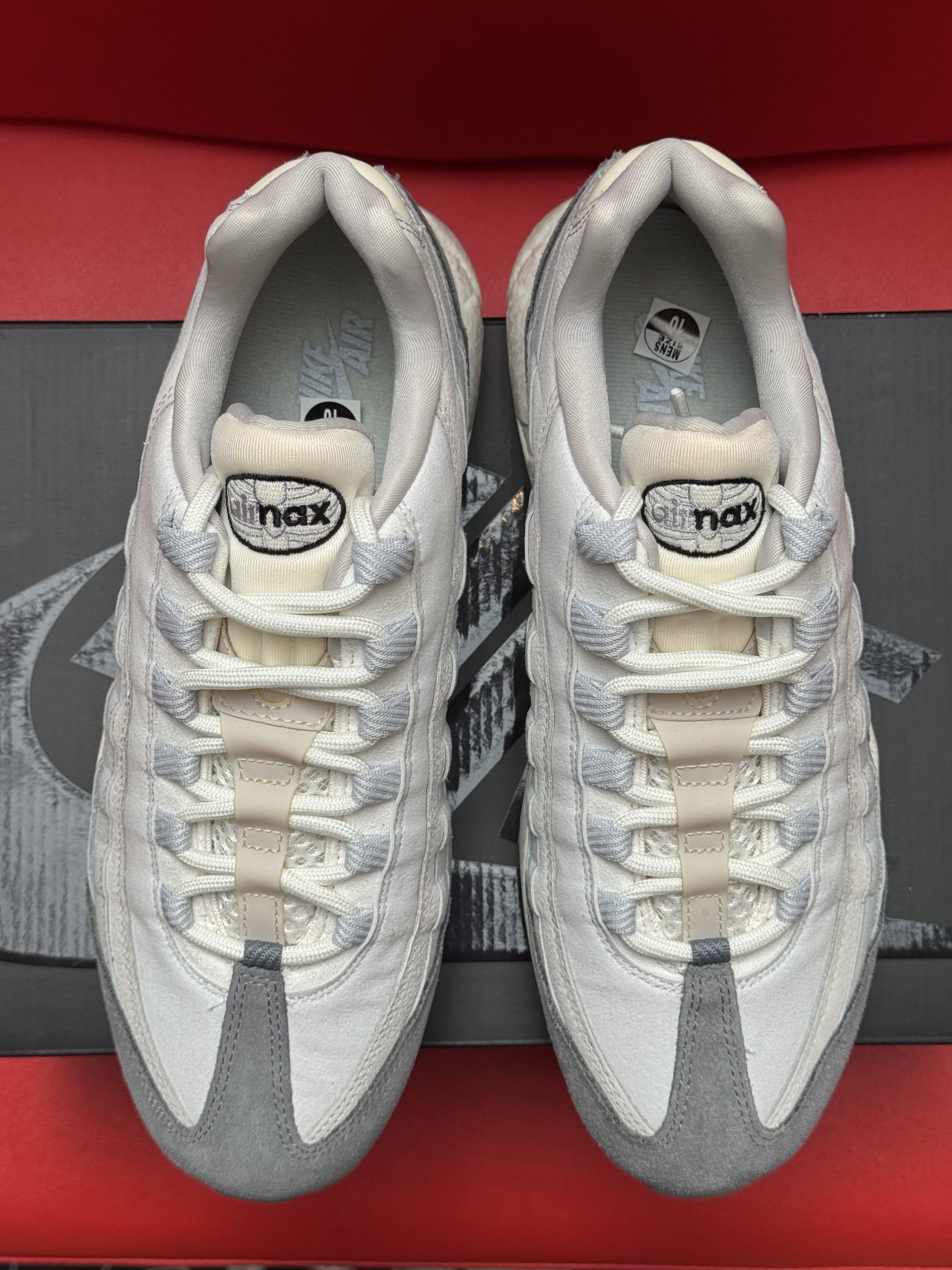 Pair of gray and white Nike Air Max 95 sneakers on a black shoebox, against a red background.