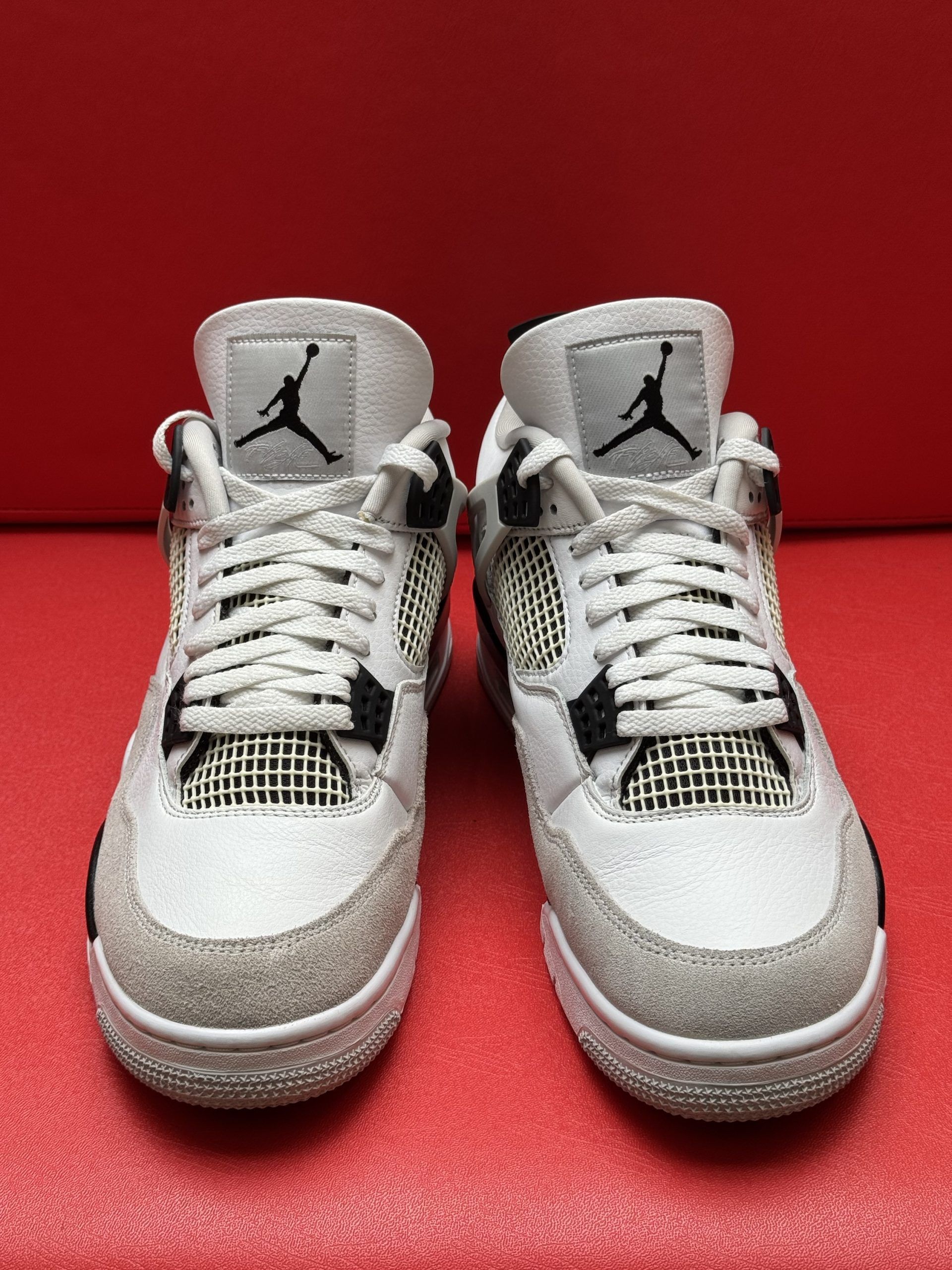 White and gray Air Jordan 4 sneakers on a red surface, with one shoe turned to show the sole.