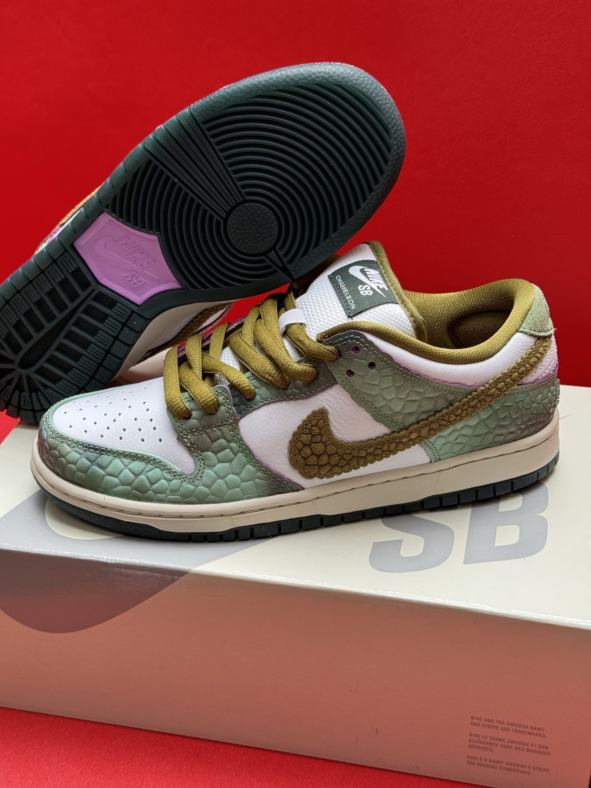 Nike SB Dunk Low sneakers in white, green, and brown, sitting on a shoebox against a red backdrop.