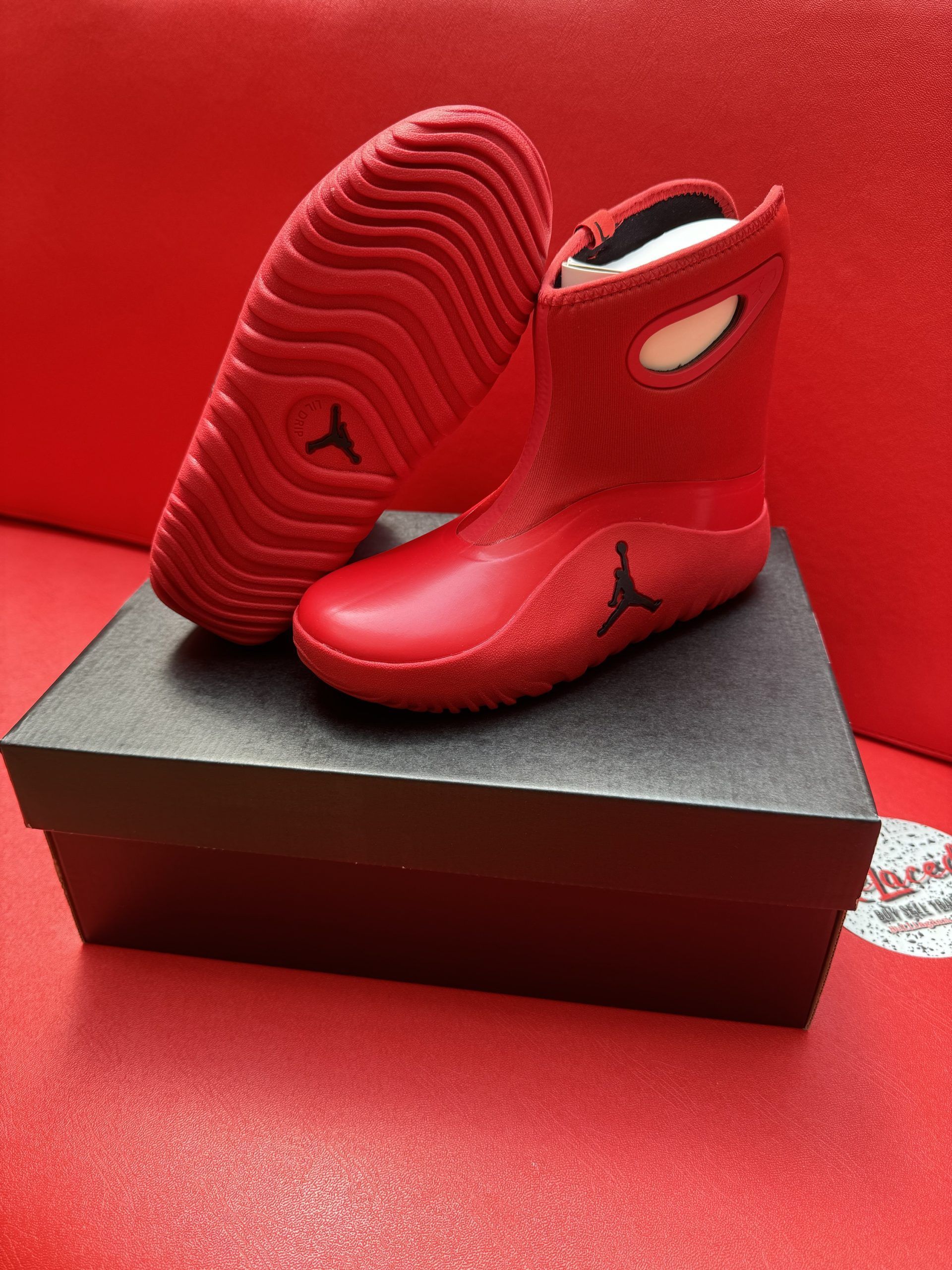 Red Jordan wrestling shoes sit on a black box against a red backdrop.