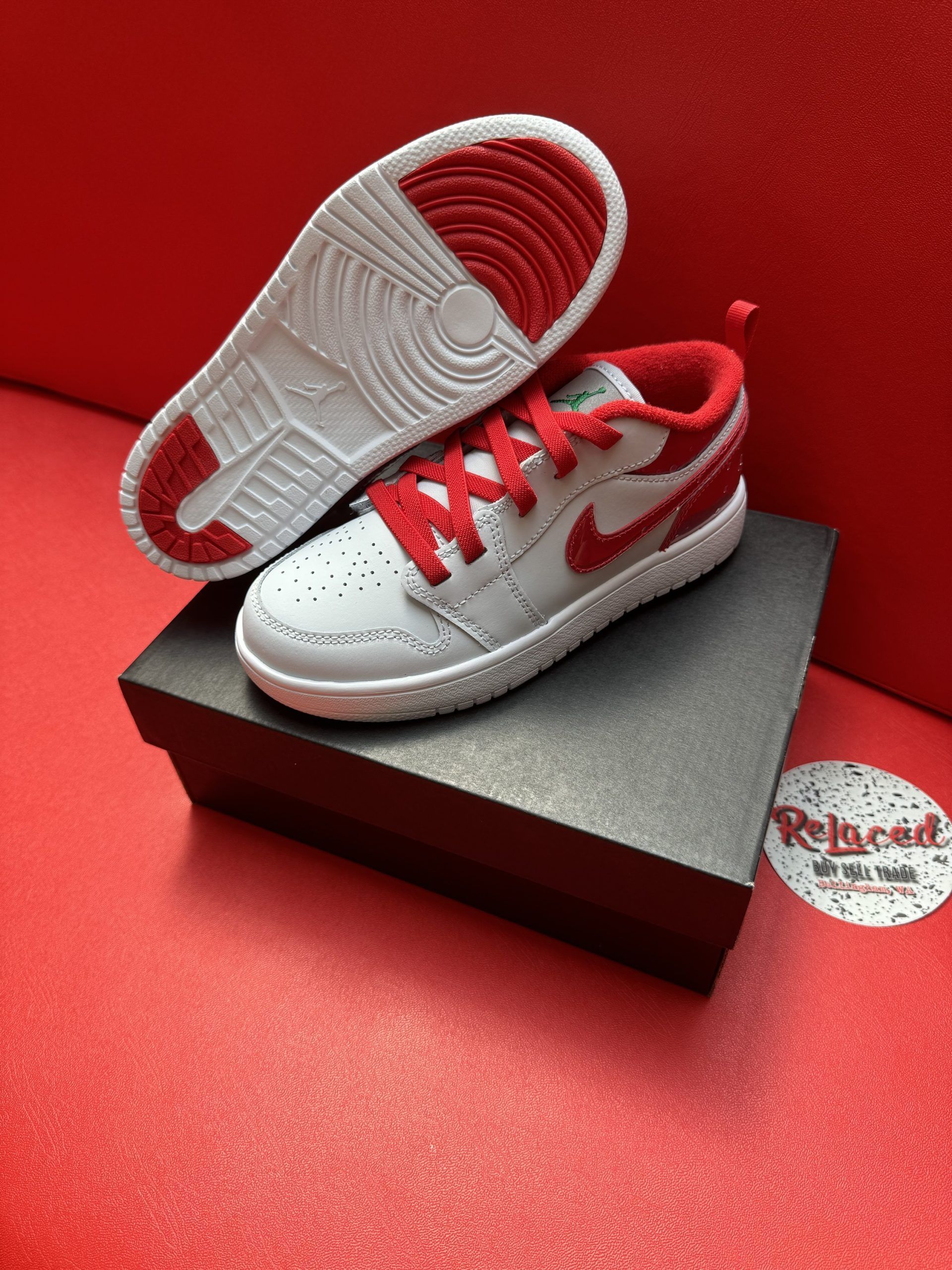 White and red children's Air Jordan sneakers on a black box, displayed against a red background.