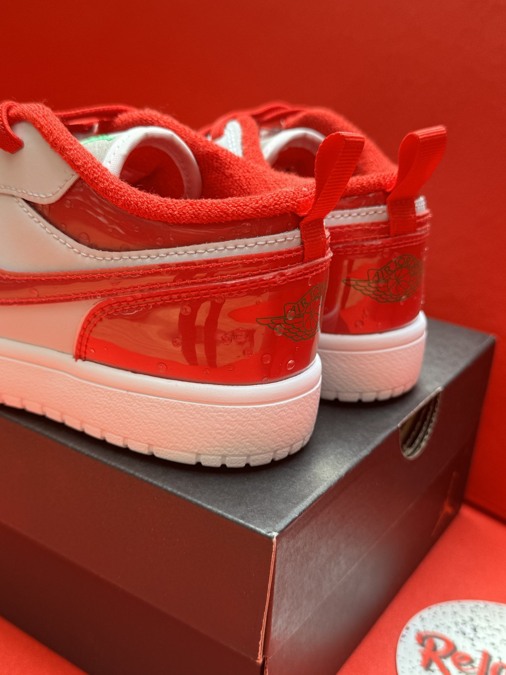 White and red children's Air Jordan sneakers on a black box, displayed against a red background.
